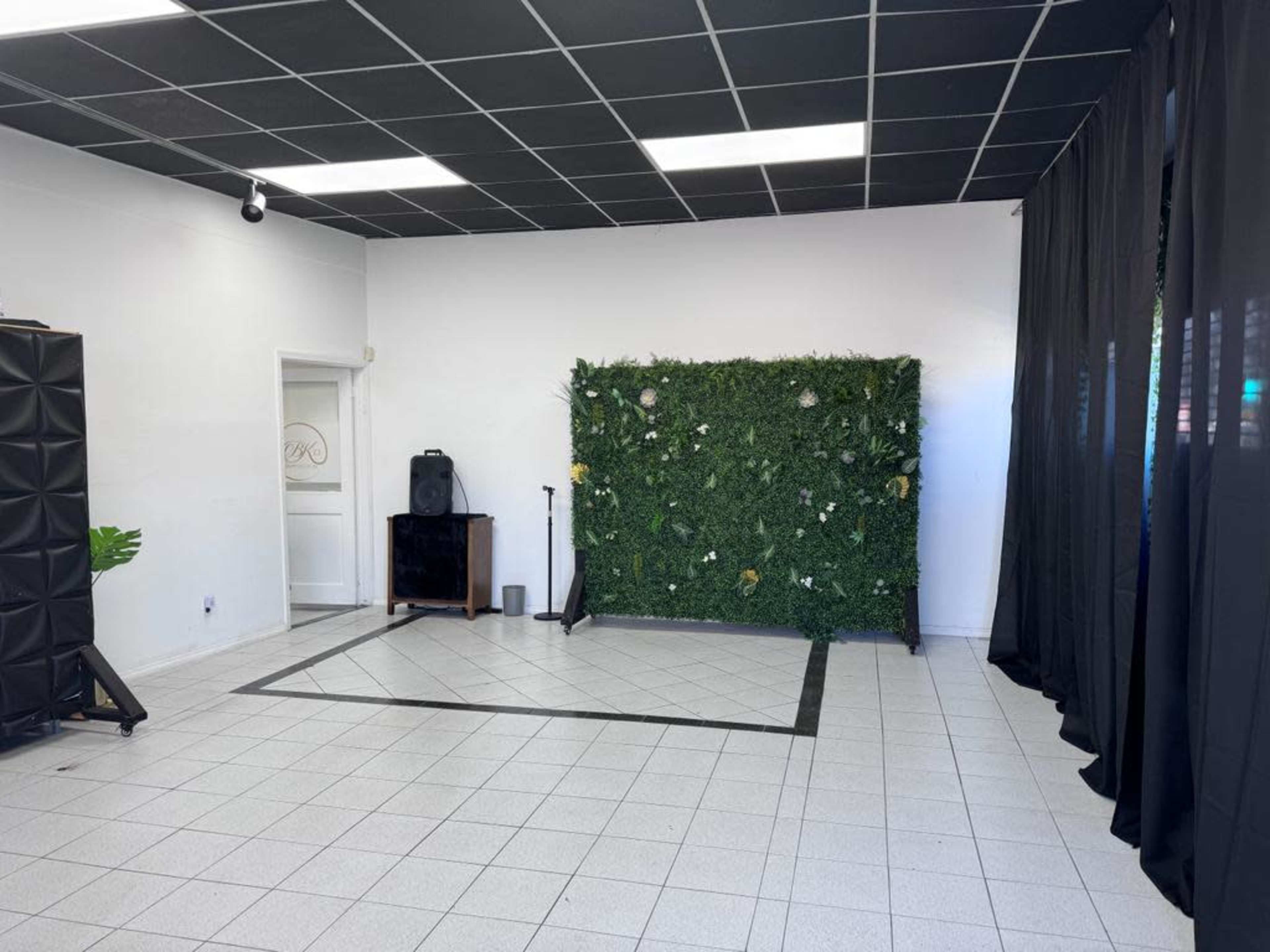 An empty room with a tiled floor, a green plant wall on one side, and black curtains along another wall.