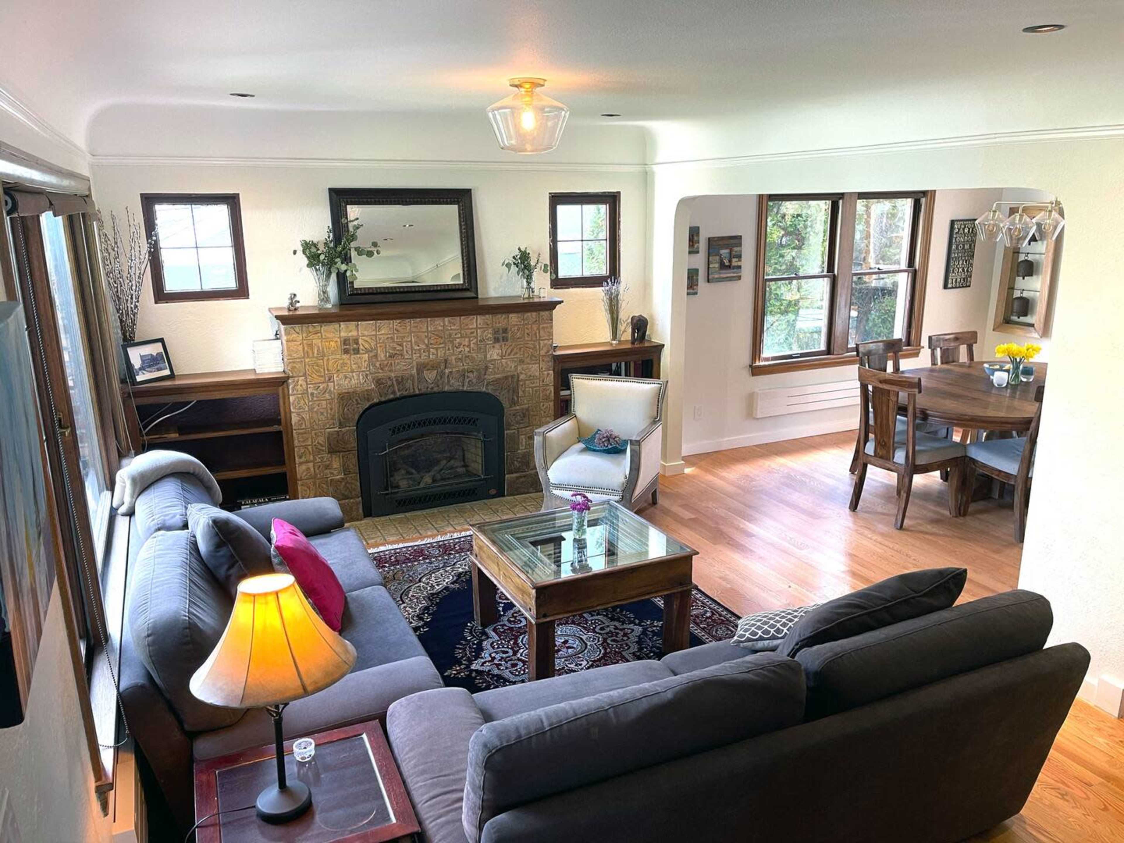 A living room with a fireplace, a gray sectional sofa, a coffee table, and a dining area with a table and chairs in an adjacent space.