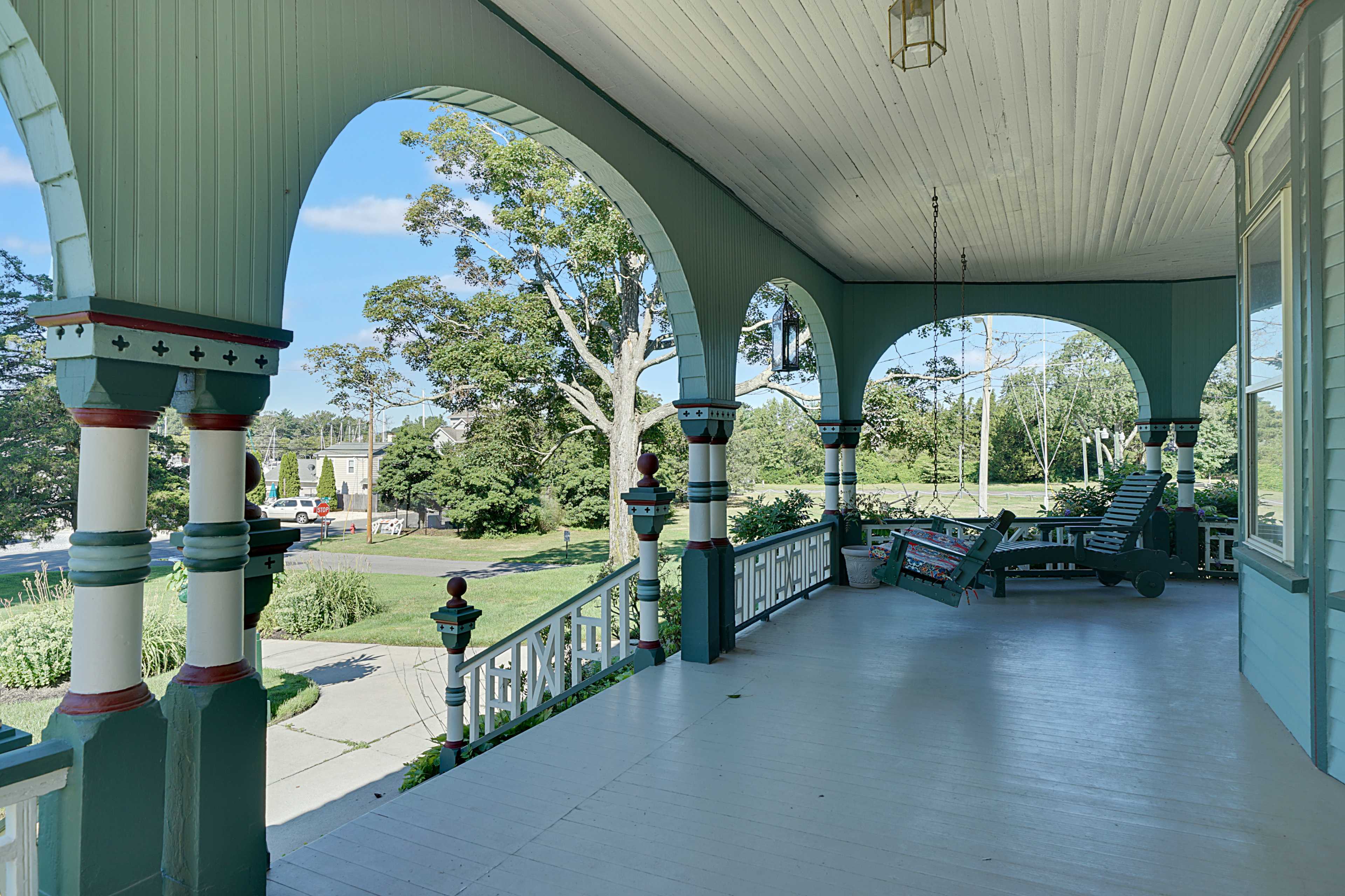 A large, covered porch with arched supports, featuring furniture and a view of a green landscape beyond.
