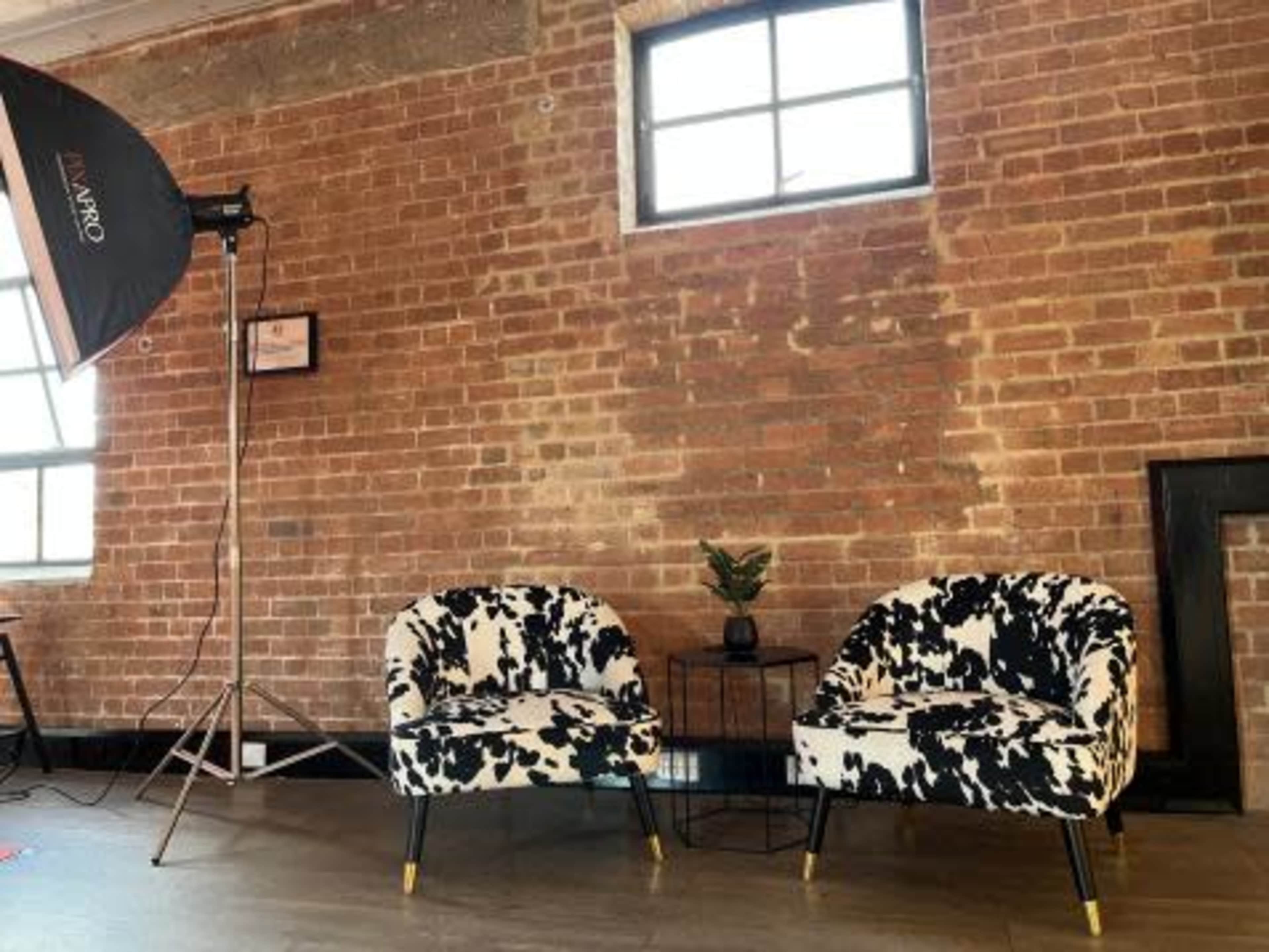 Two patterned chairs placed next to a small table against a backdrop of a brick wall and a window.