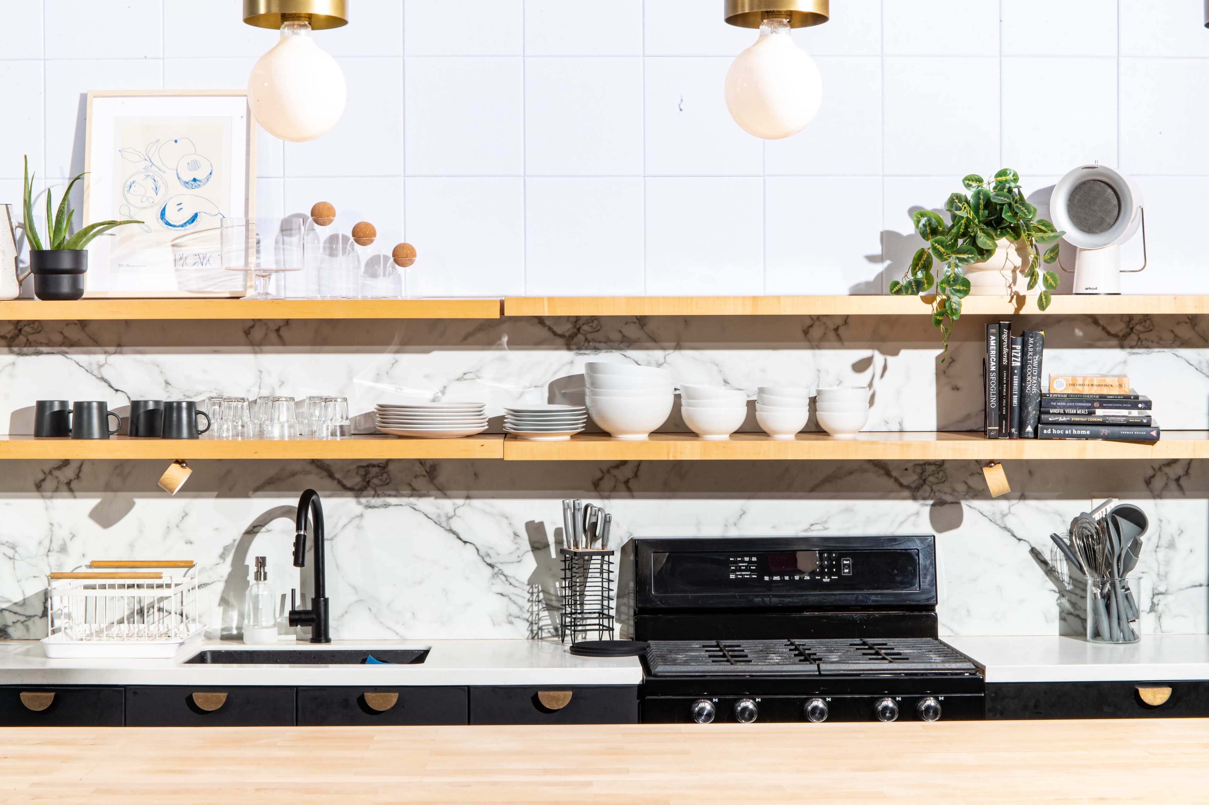 A modern kitchen with open shelving displaying dishes, plants, and kitchen tools above a black stove and sink.