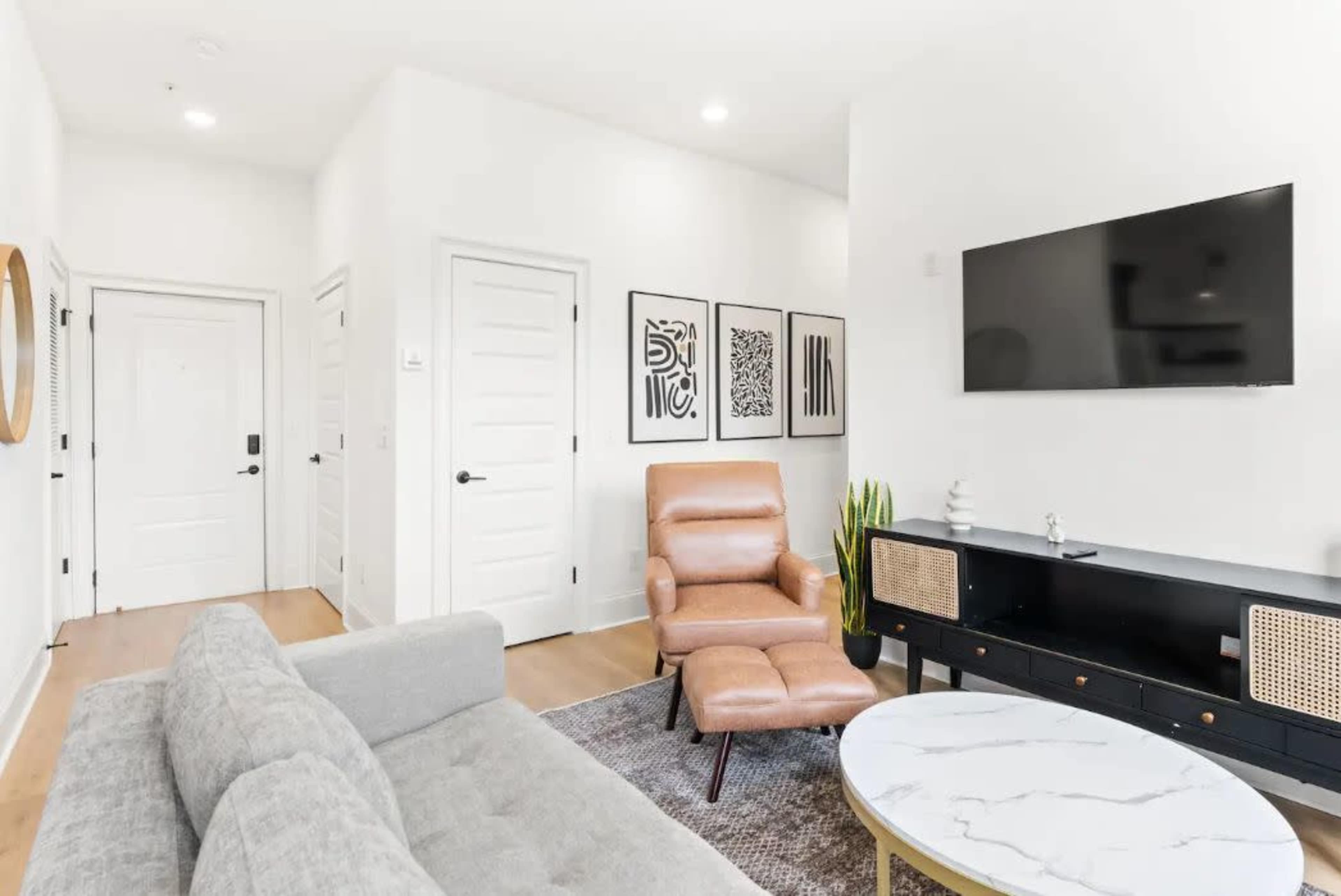 A modern living room features a gray sofa, an armchair, a decorative television on the wall, and framed artwork.