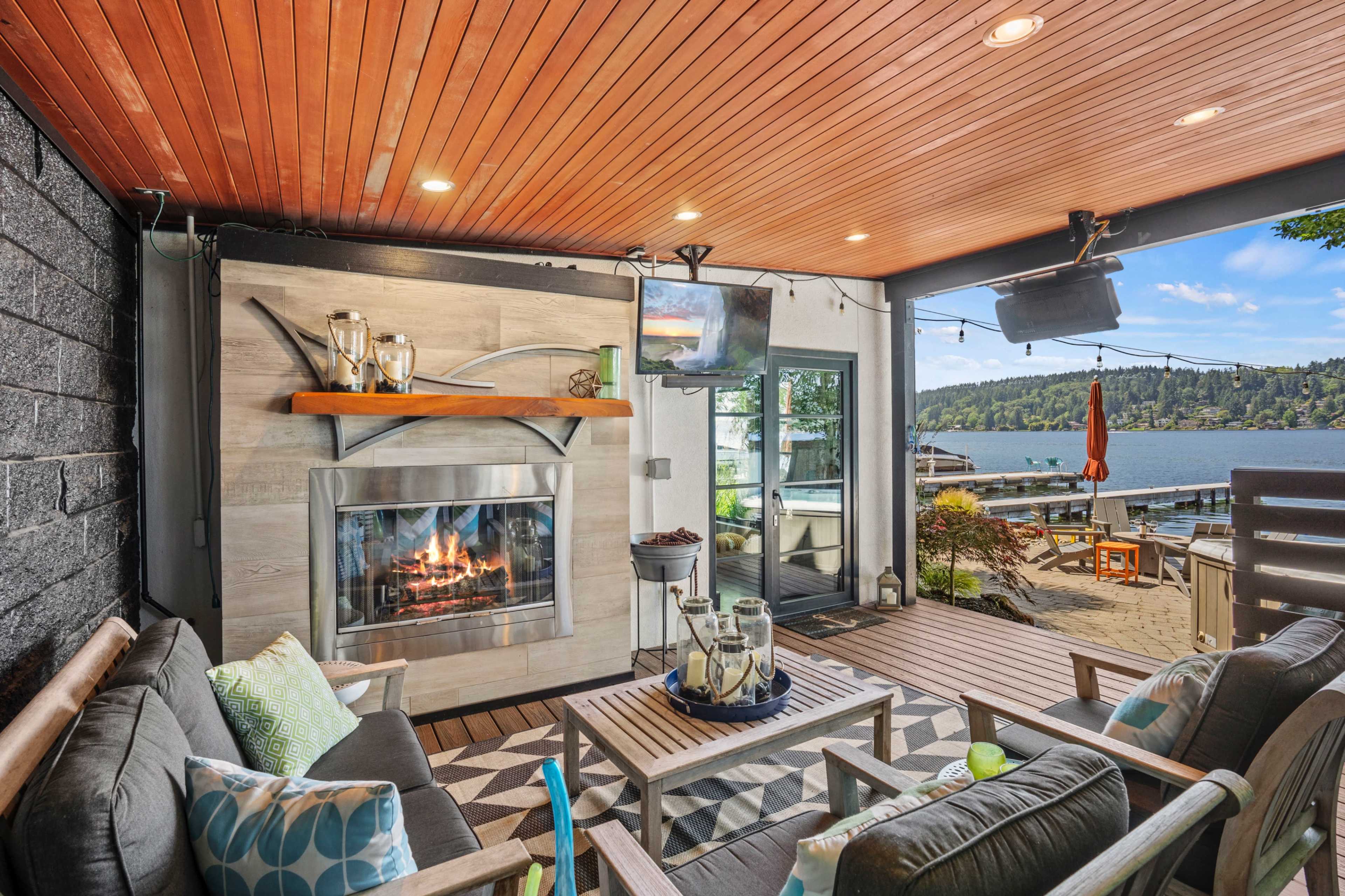 A covered outdoor living area with a fireplace, comfortable seating, and a view of a lake.