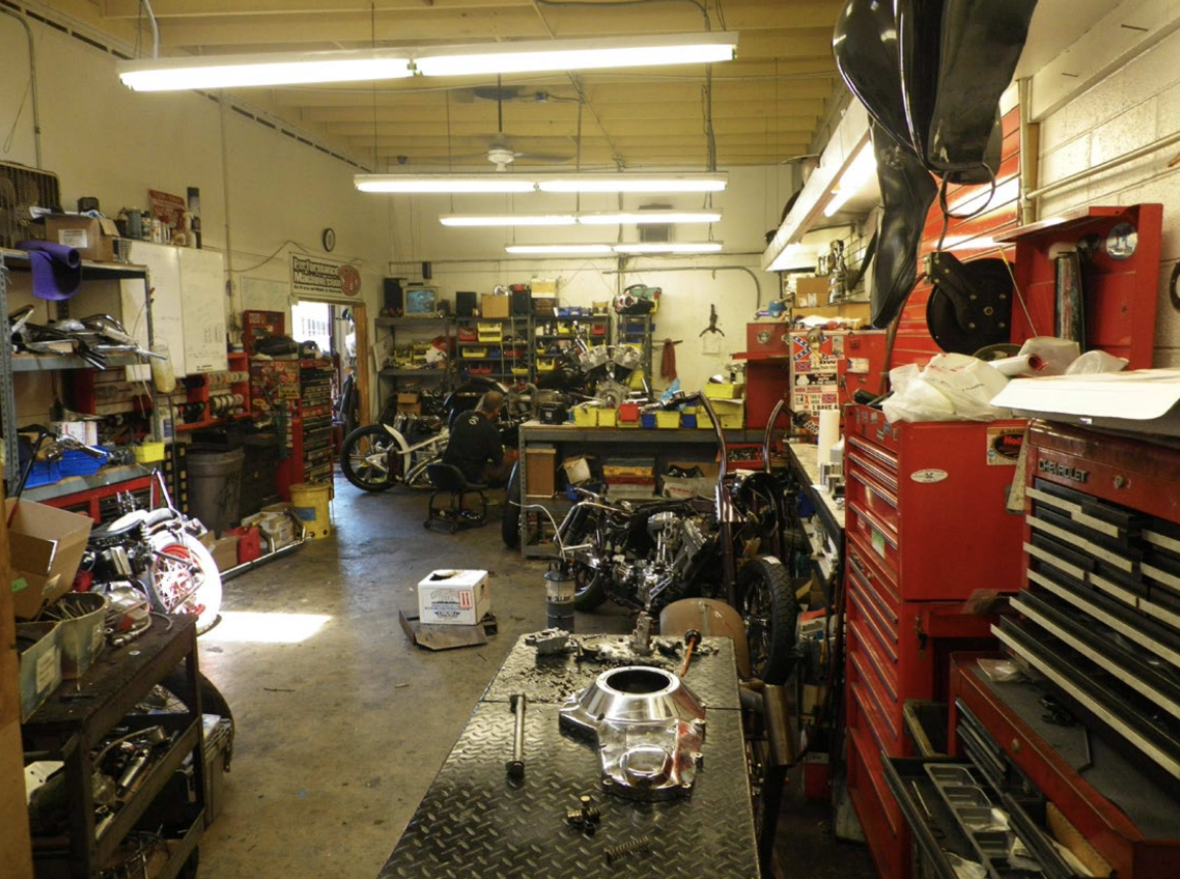 The image shows a cluttered garage workshop filled with tools, parts, and motorcycle frames.