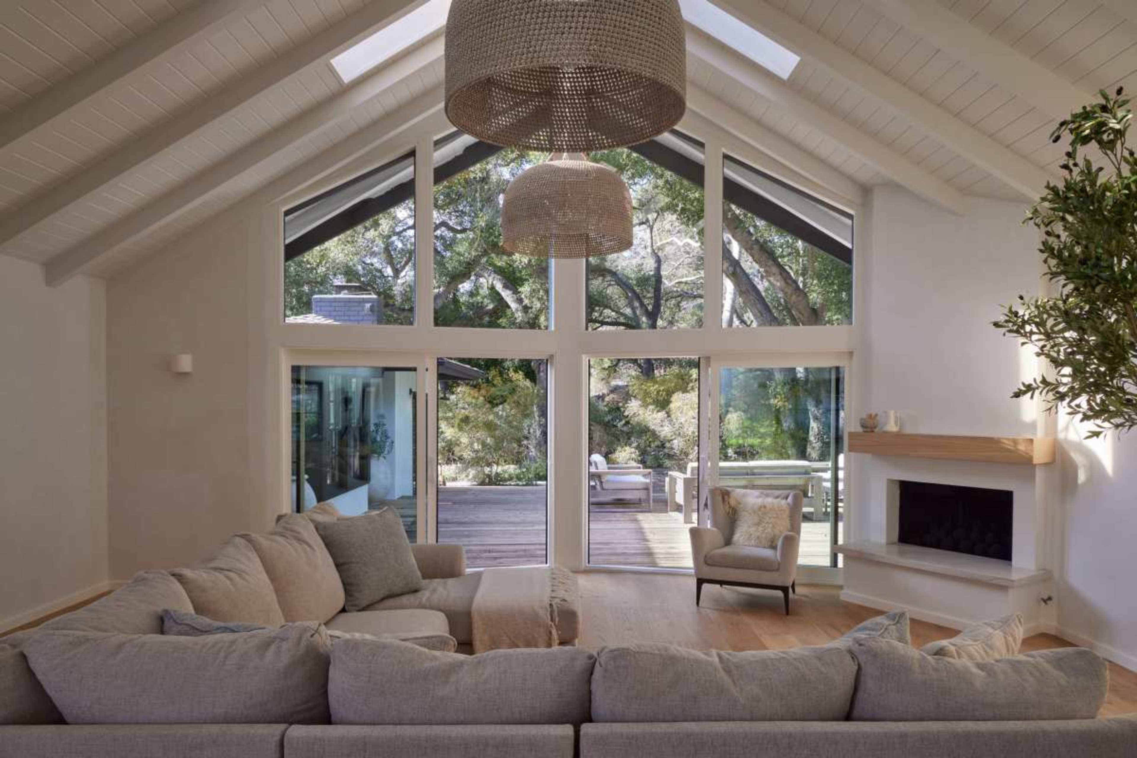 The spacious living room features a large sectional sofa facing a fireplace, with large windows that provide a view of the outdoor area.