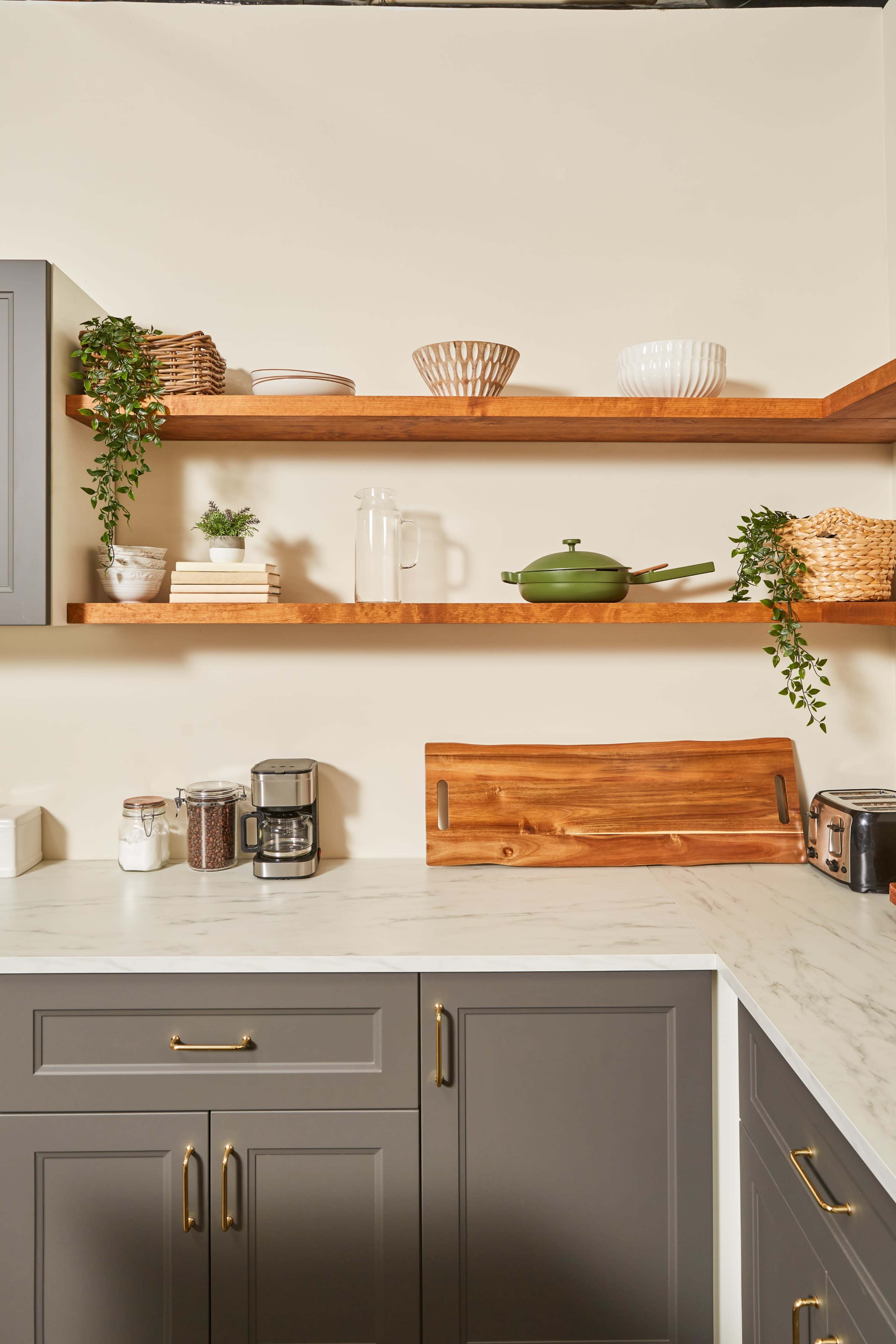 A modern kitchen with gray cabinets, wooden shelves holding decorative items, and a coffee maker on the countertop.