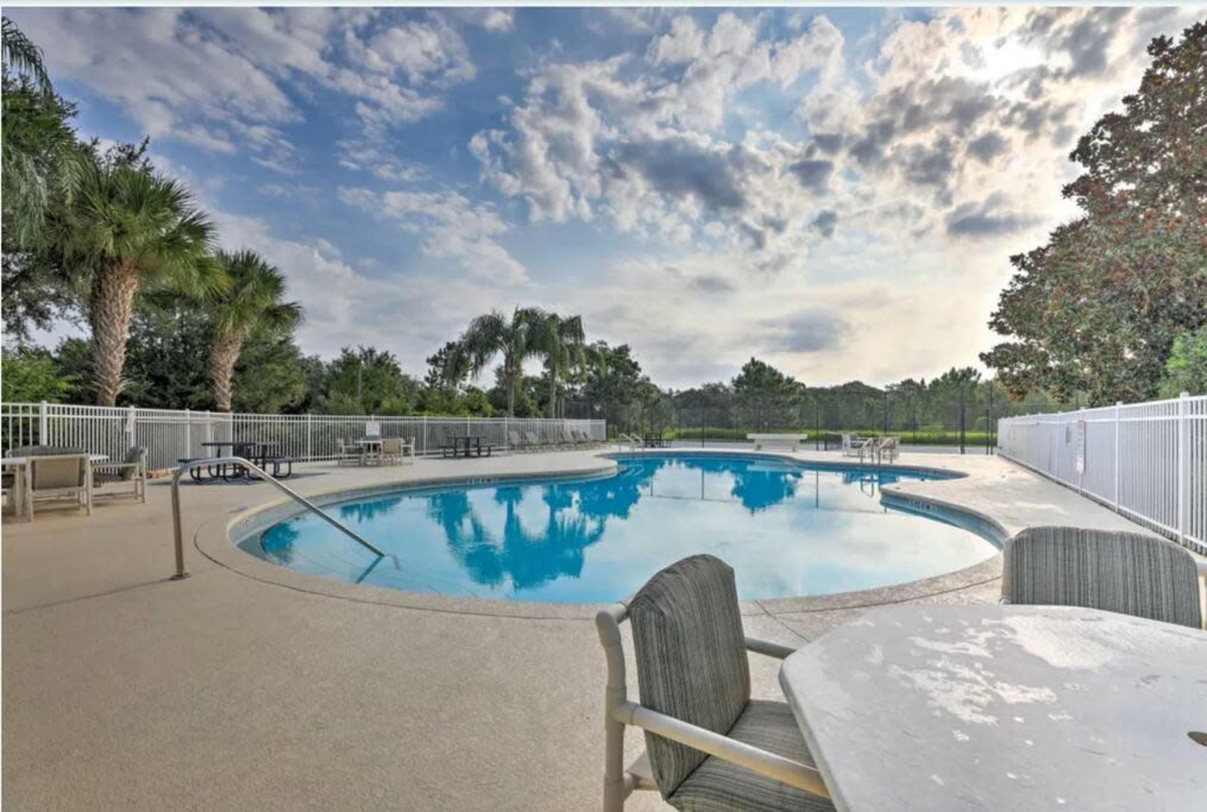 A clean swimming pool surrounded by lounge chairs and palm trees is set against a cloudy sky.