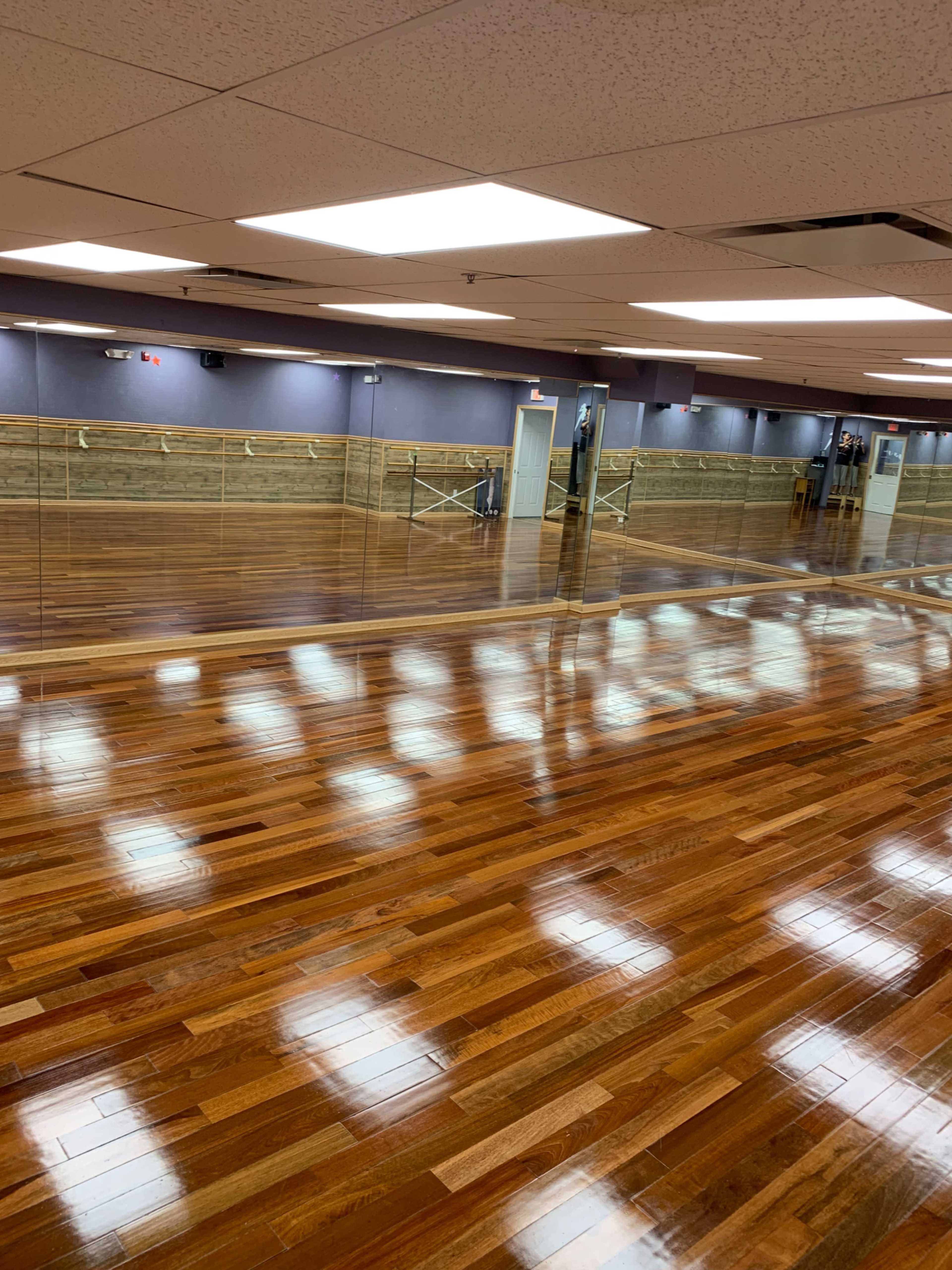 A spacious wooden dance studio with polished floors and mirrored walls.