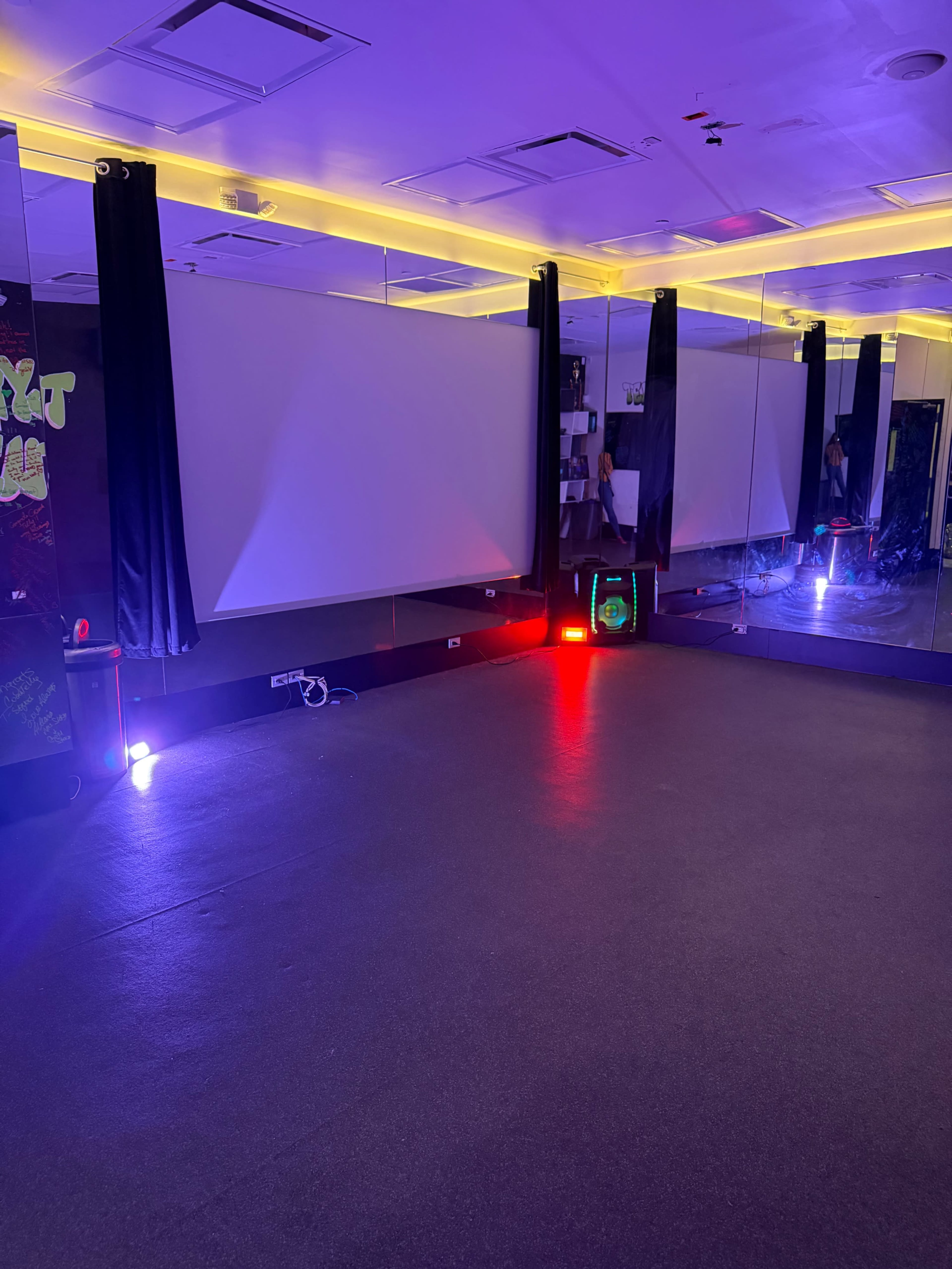 The image shows a dimly lit dance studio with mirrored walls and colorful lighting fixtures in the corners.