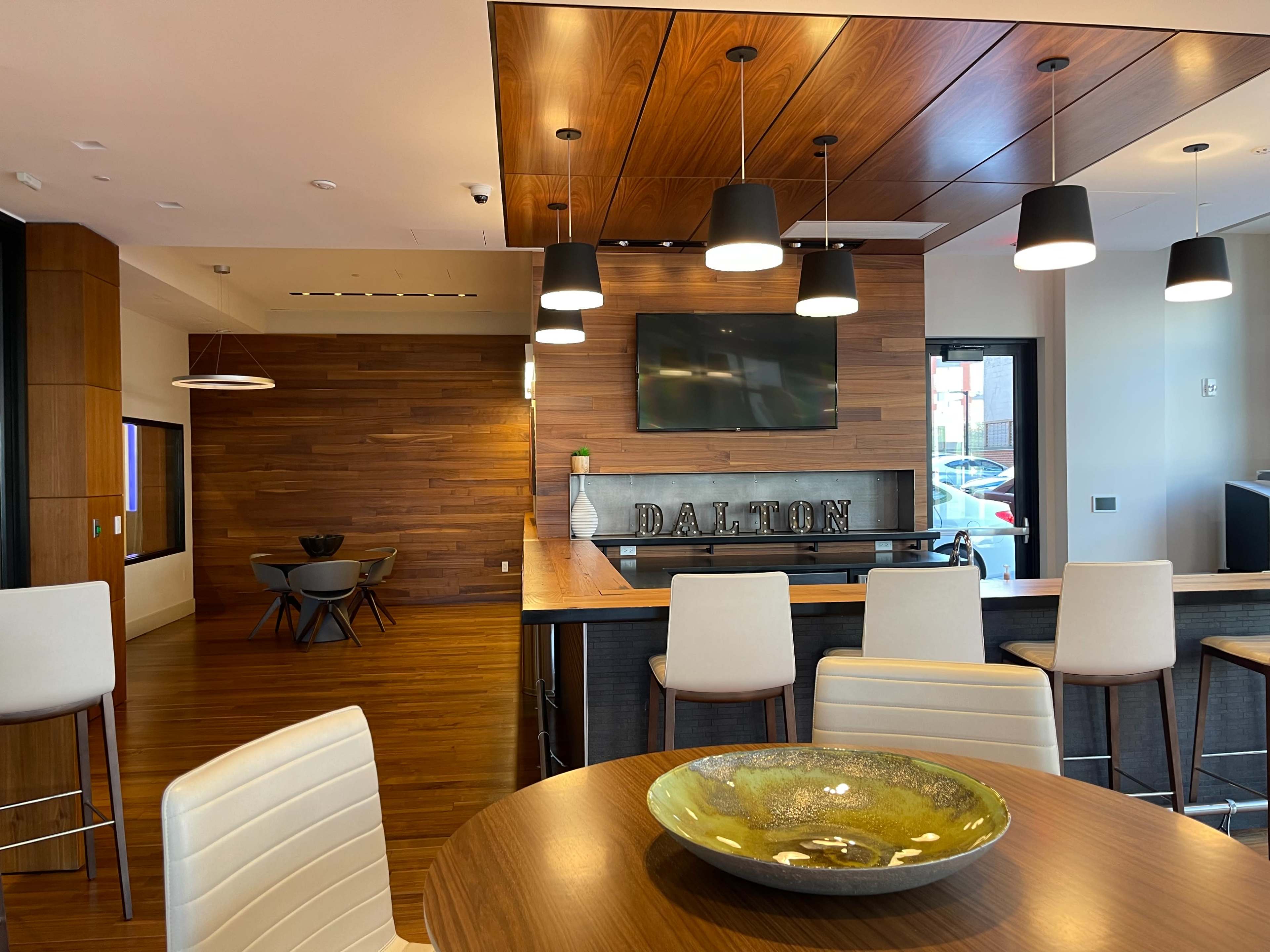A modern interior space with wooden paneling, a bar area with stools, and a dining table featuring a large decorative bowl.