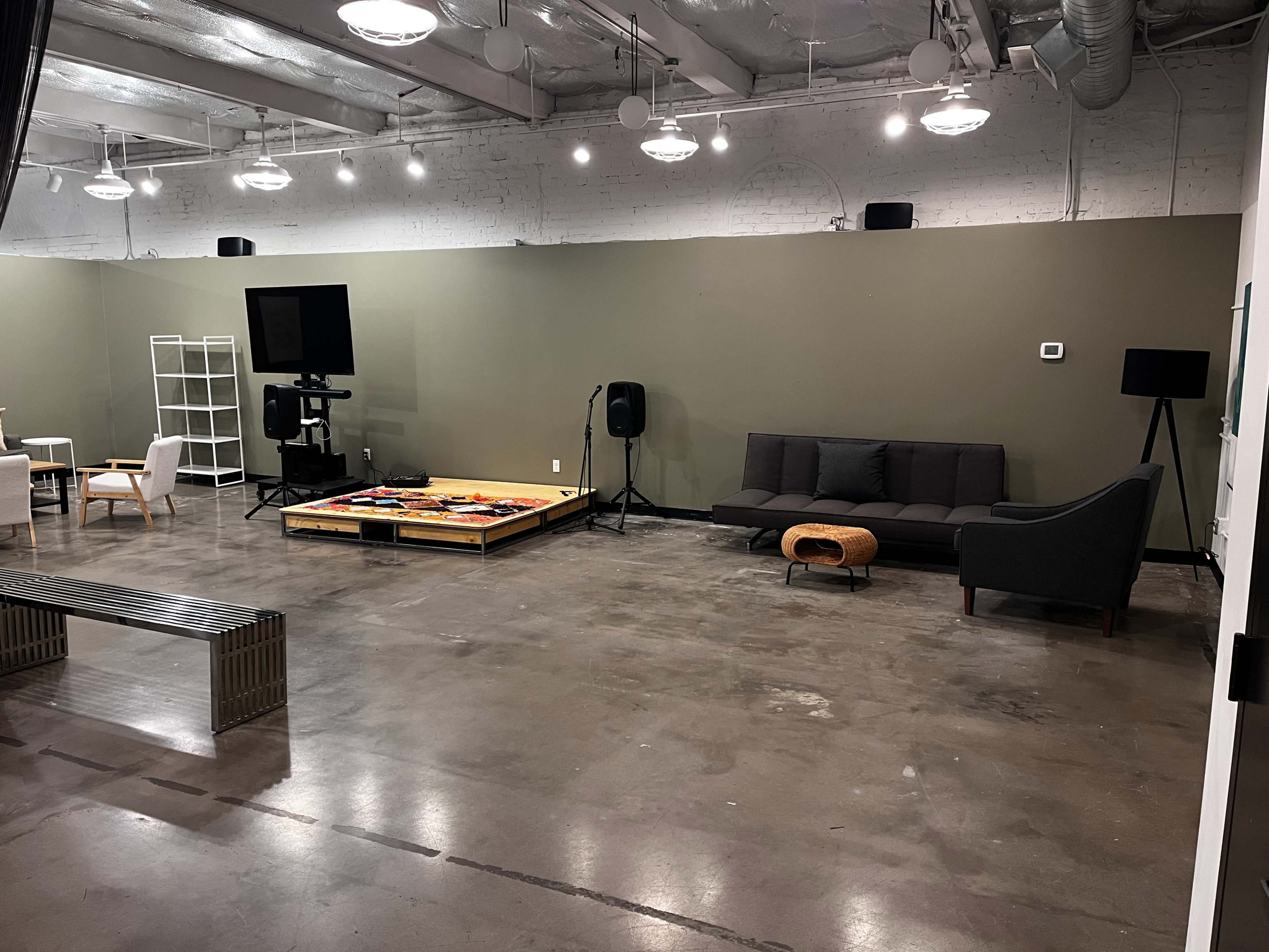 The image shows a spacious, modern room with a few pieces of furniture, including a couch, a coffee table, and a television setup on a platform.