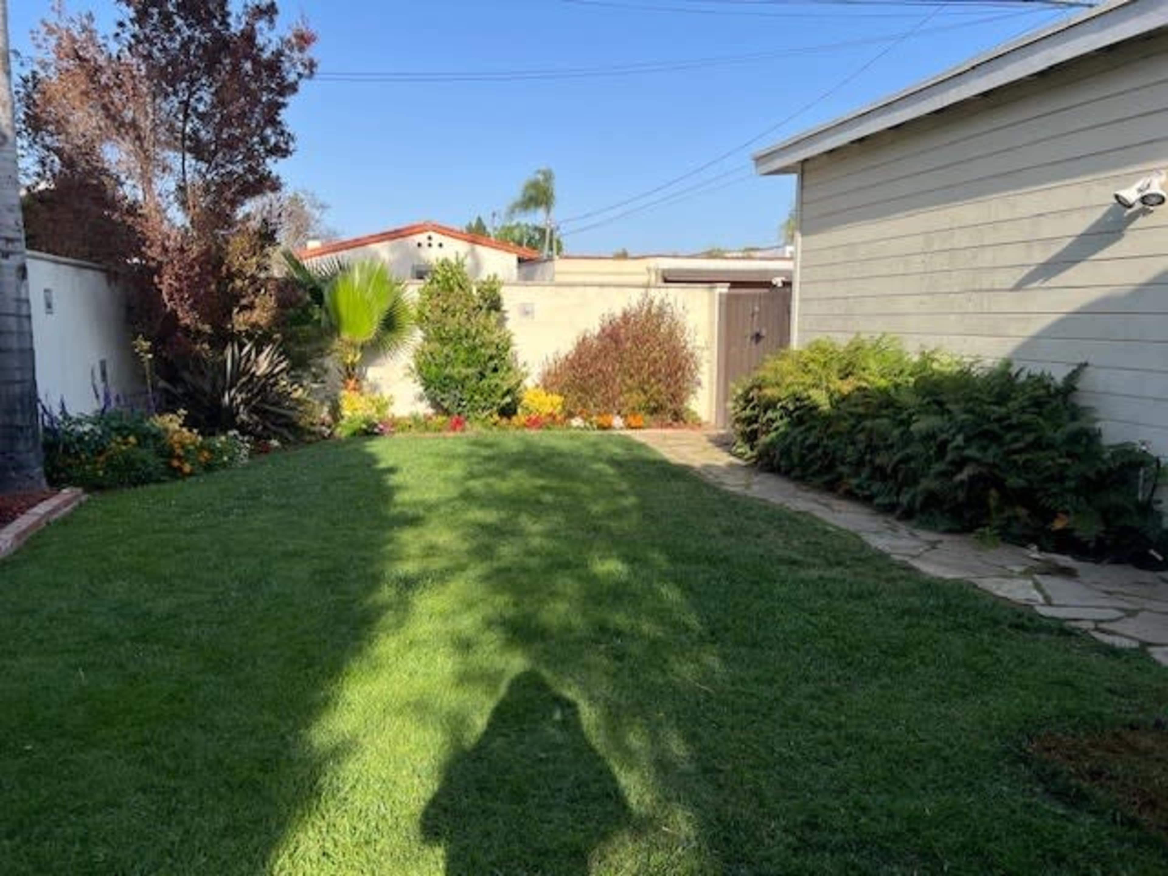 A landscaped backyard featuring a grassy area, flower beds, a pathway, and a building on the right side.