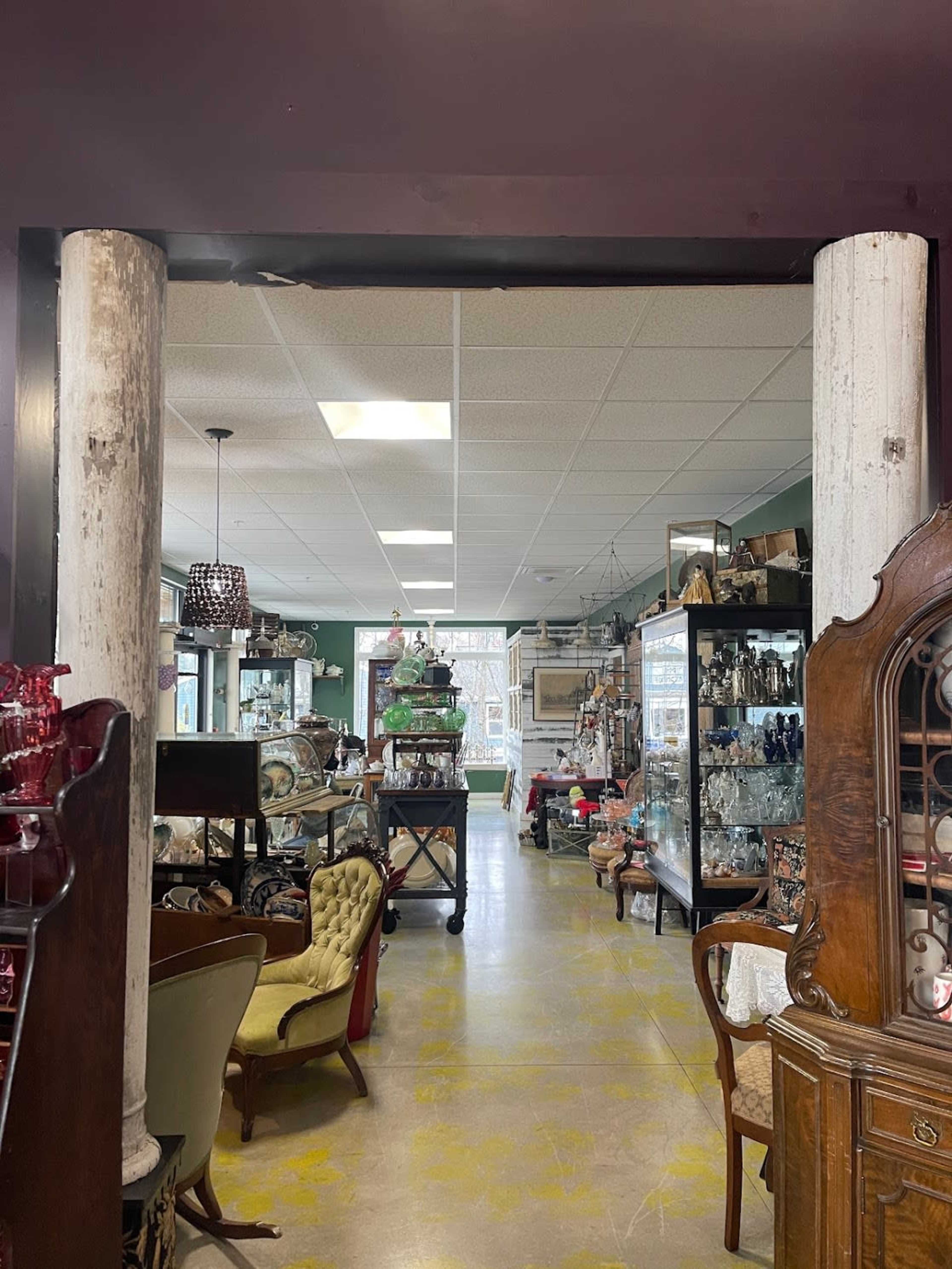 A vintage shop interior with various antique items displayed along the aisles, framed by two white columns at the entrance.