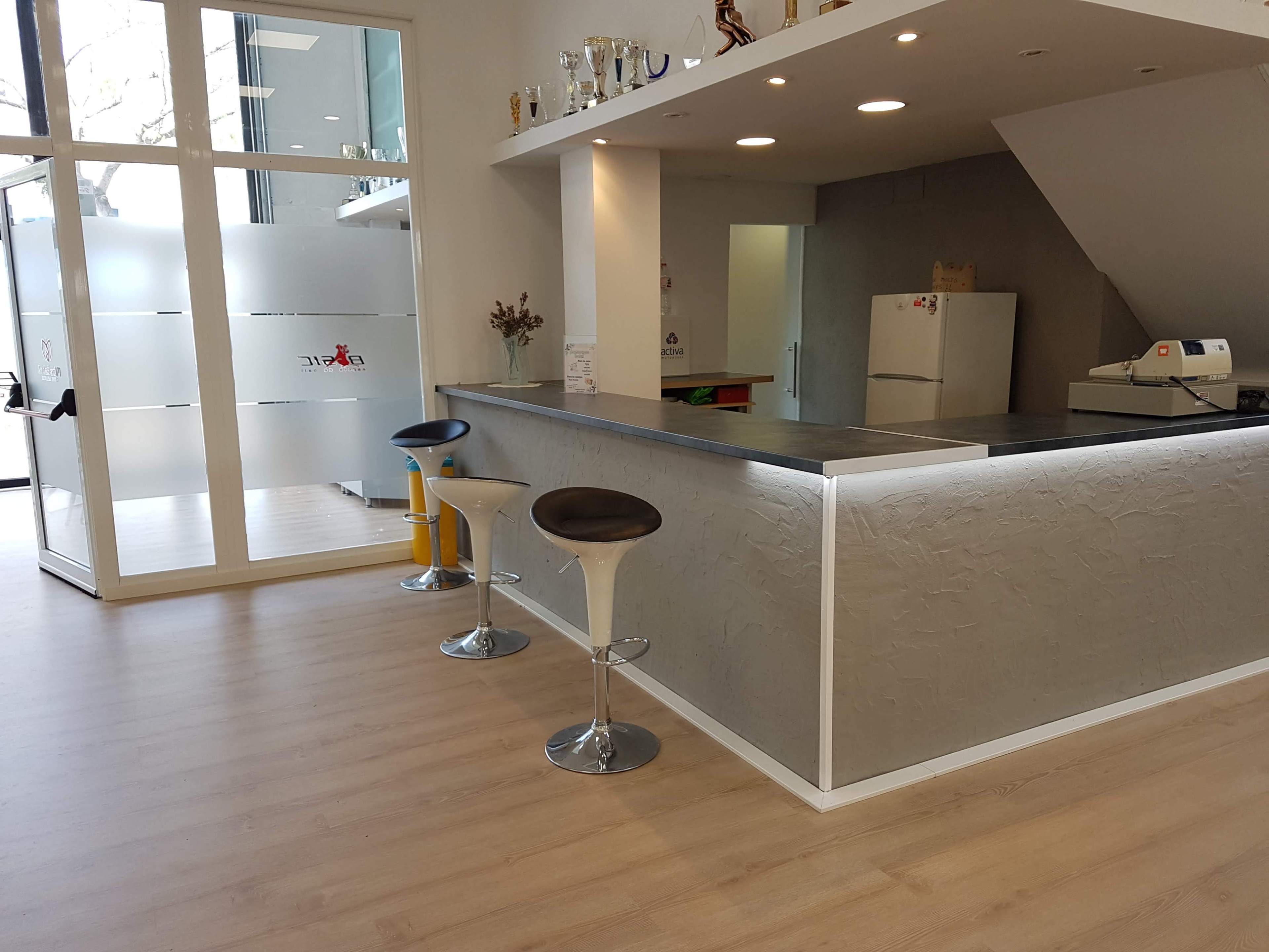 A modern interior space featuring a counter with bar stools, a kitchen area, and a large window with frosted glass.