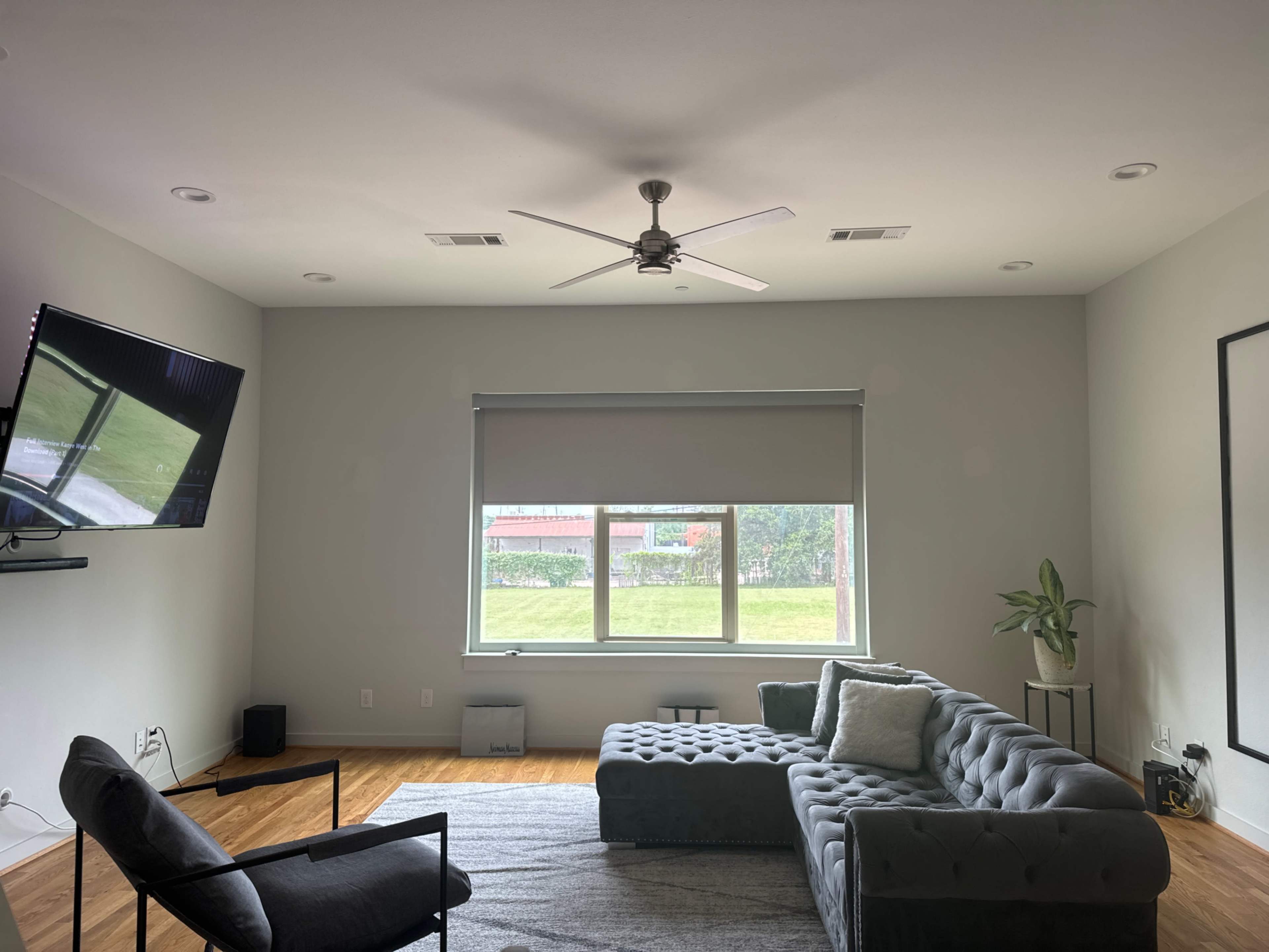 A spacious living room featuring a sectional sofa, a television mounted on the wall, and a large window with a view of greenery outside.