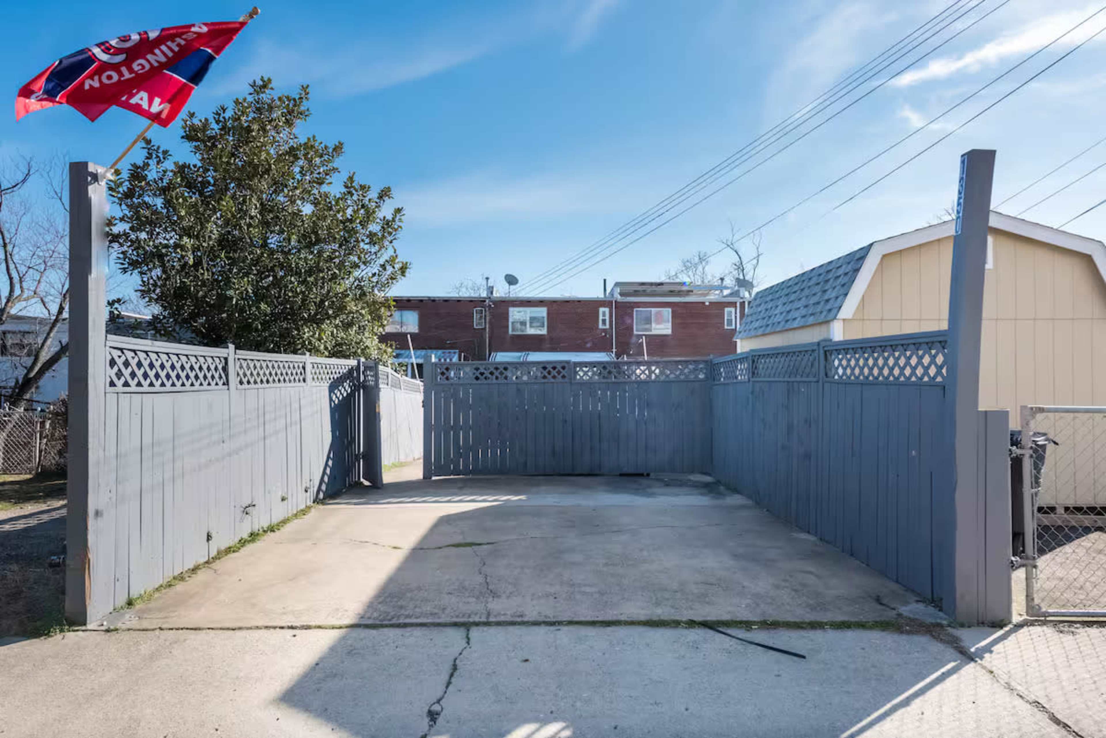 The image shows a fenced outdoor area with a concrete surface, surrounded by gray wooden fences and a yellow building in the background.