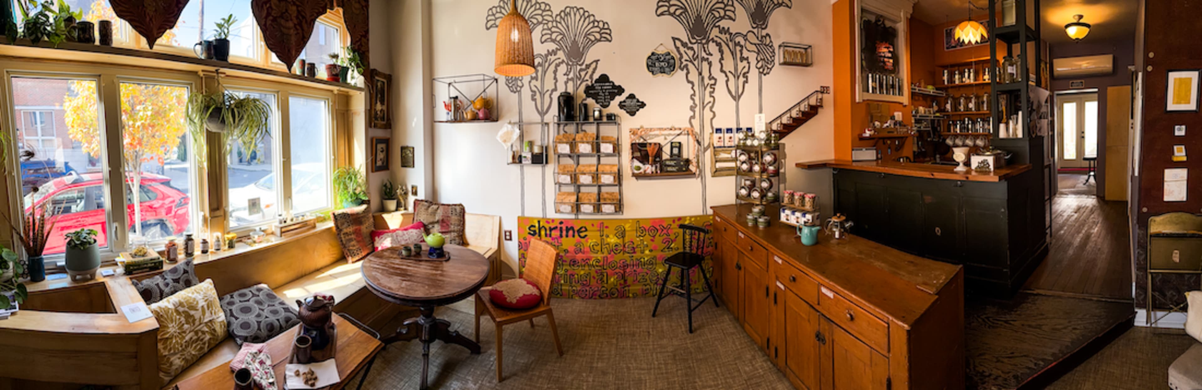 The image depicts a cozy café interior with various seating options, light wood furniture, and a decorative wall featuring a tree mural.