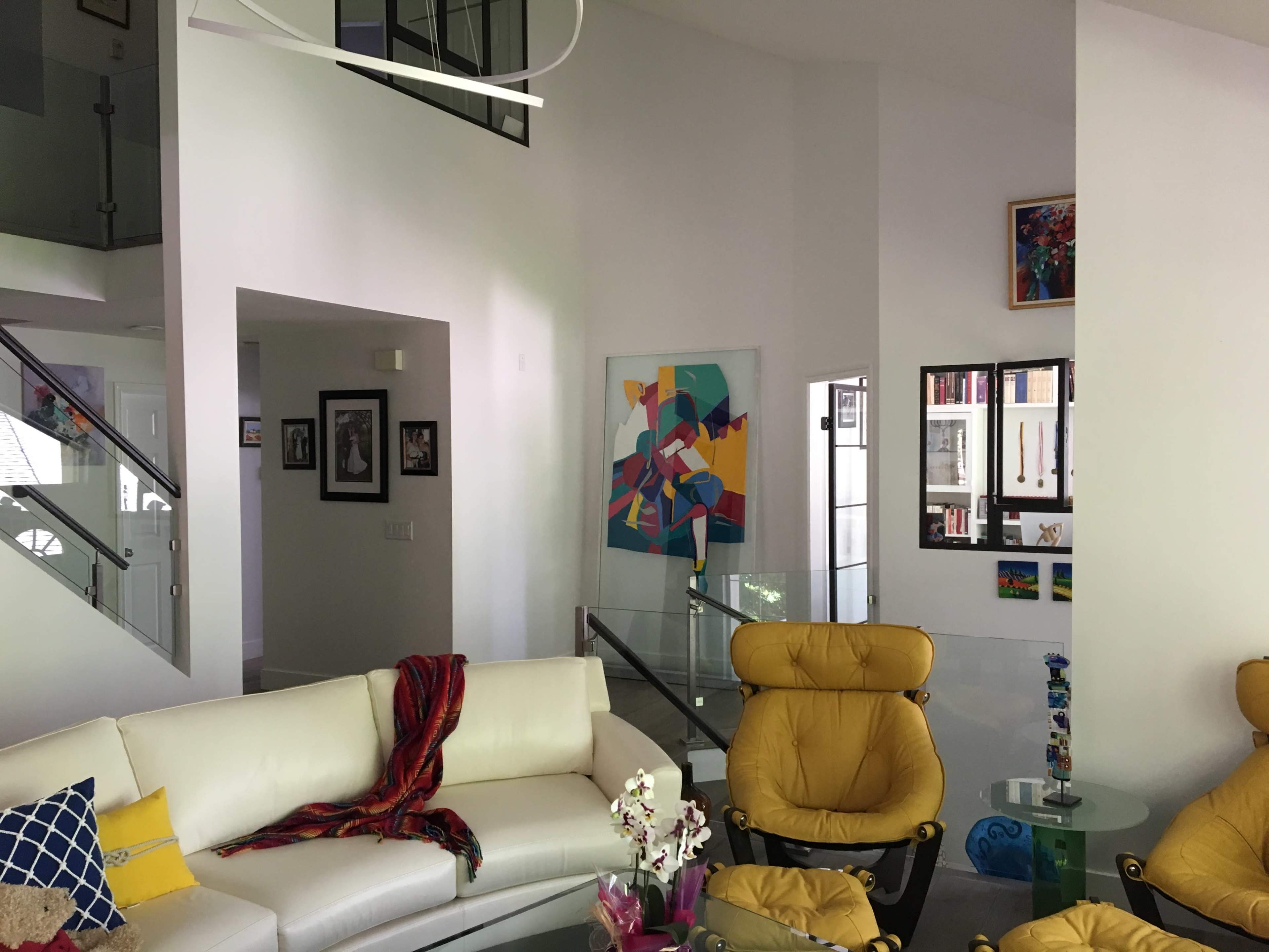 A modern living room features a white sectional sofa, yellow armchairs, and colorful wall art amidst a bright, open layout.
