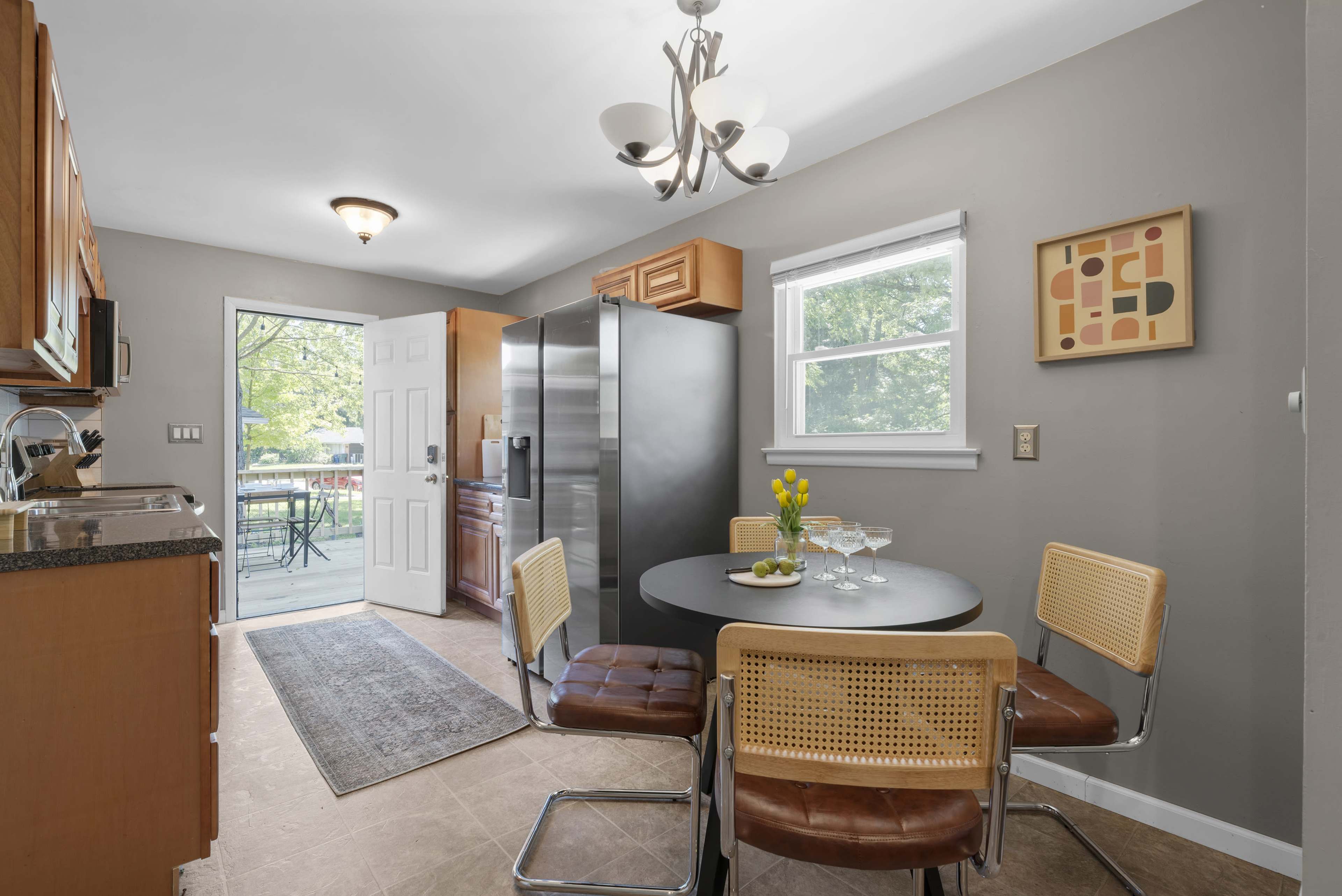 A modern kitchen features a circular table with four chairs, a stainless steel refrigerator, and a door leading to an outdoor area.