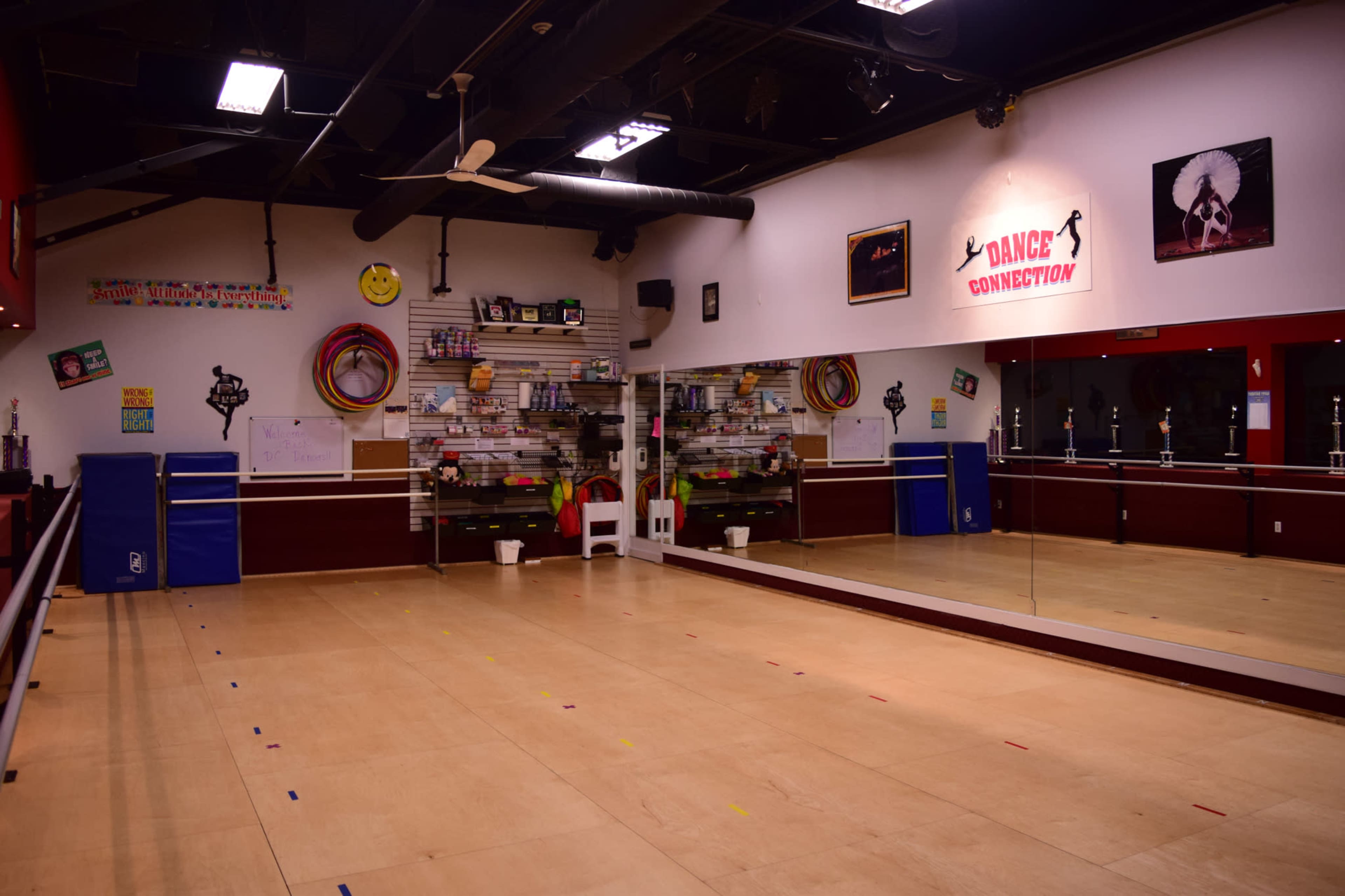 A dance studio with a wooden floor, mirrored walls, and various dance trophies displayed on shelves.