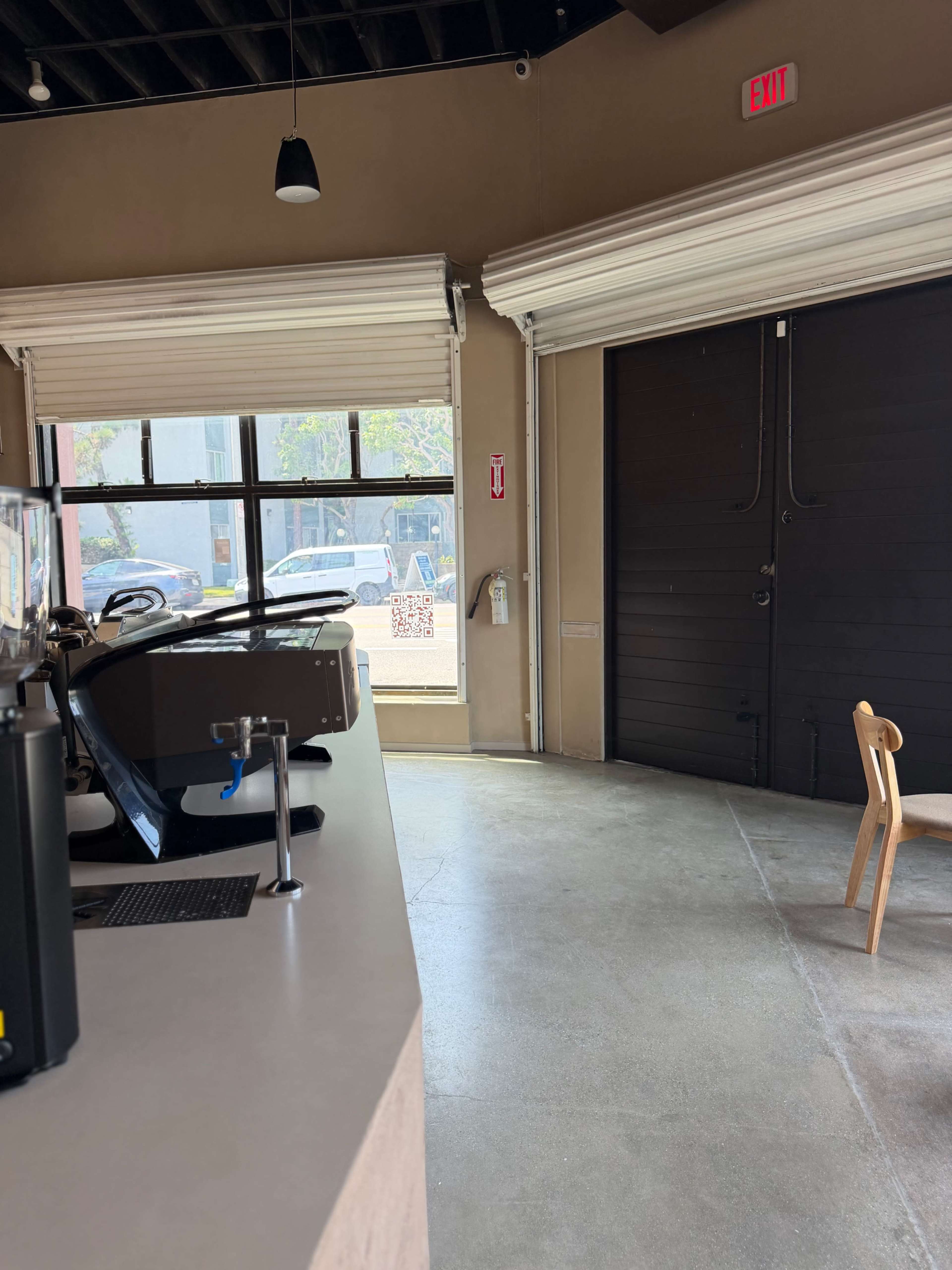 The image shows the interior of a café with a counter on the left, a large window in the center, and a closed door on the right.