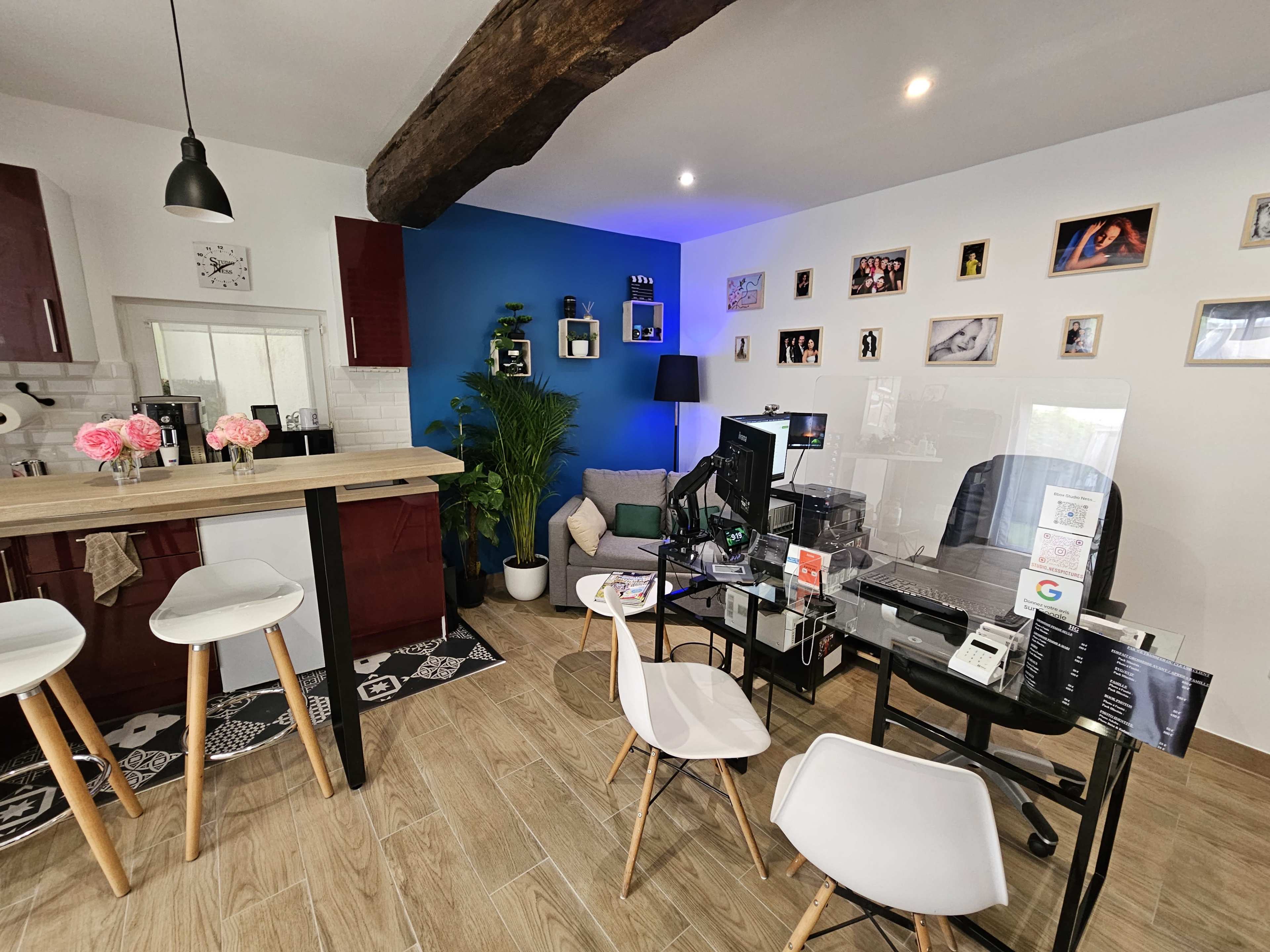 A modern workspace with a desk, computer, and chairs, set against a blue accent wall and decorated with framed photos and a plant.