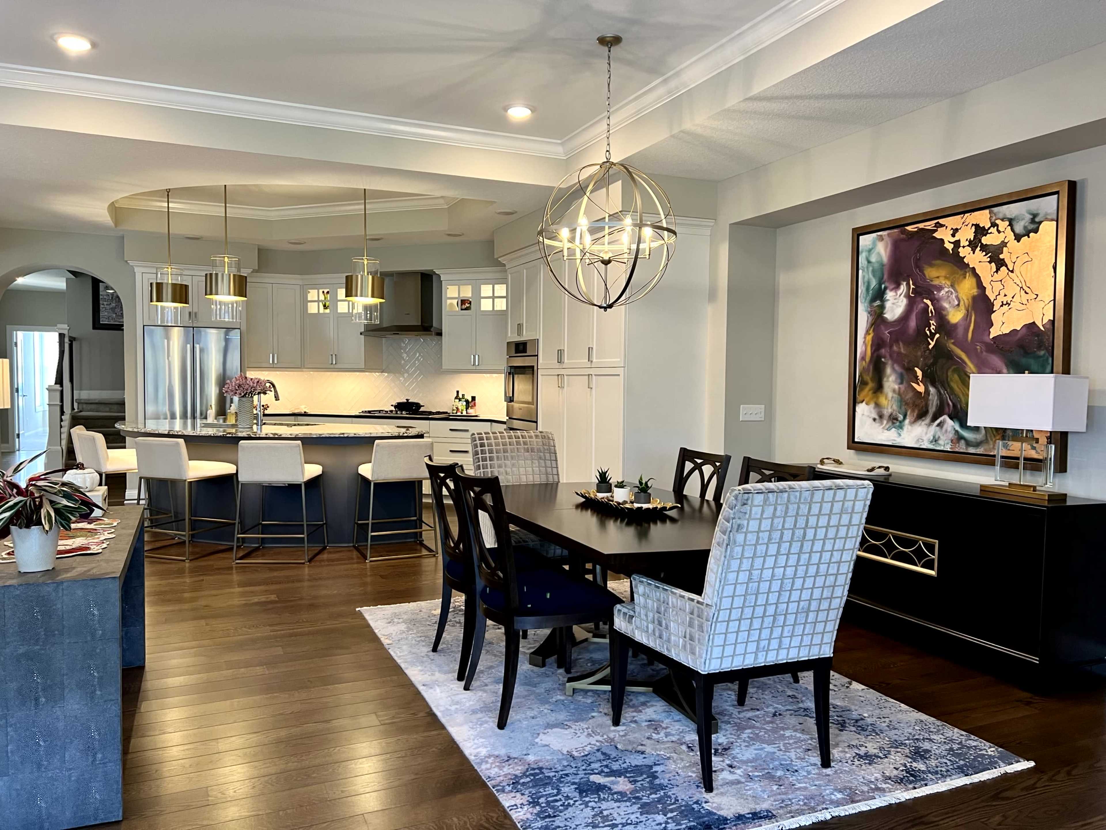 A modern kitchen and dining area feature a central island, stylish dining furniture, and artistic wall decor.