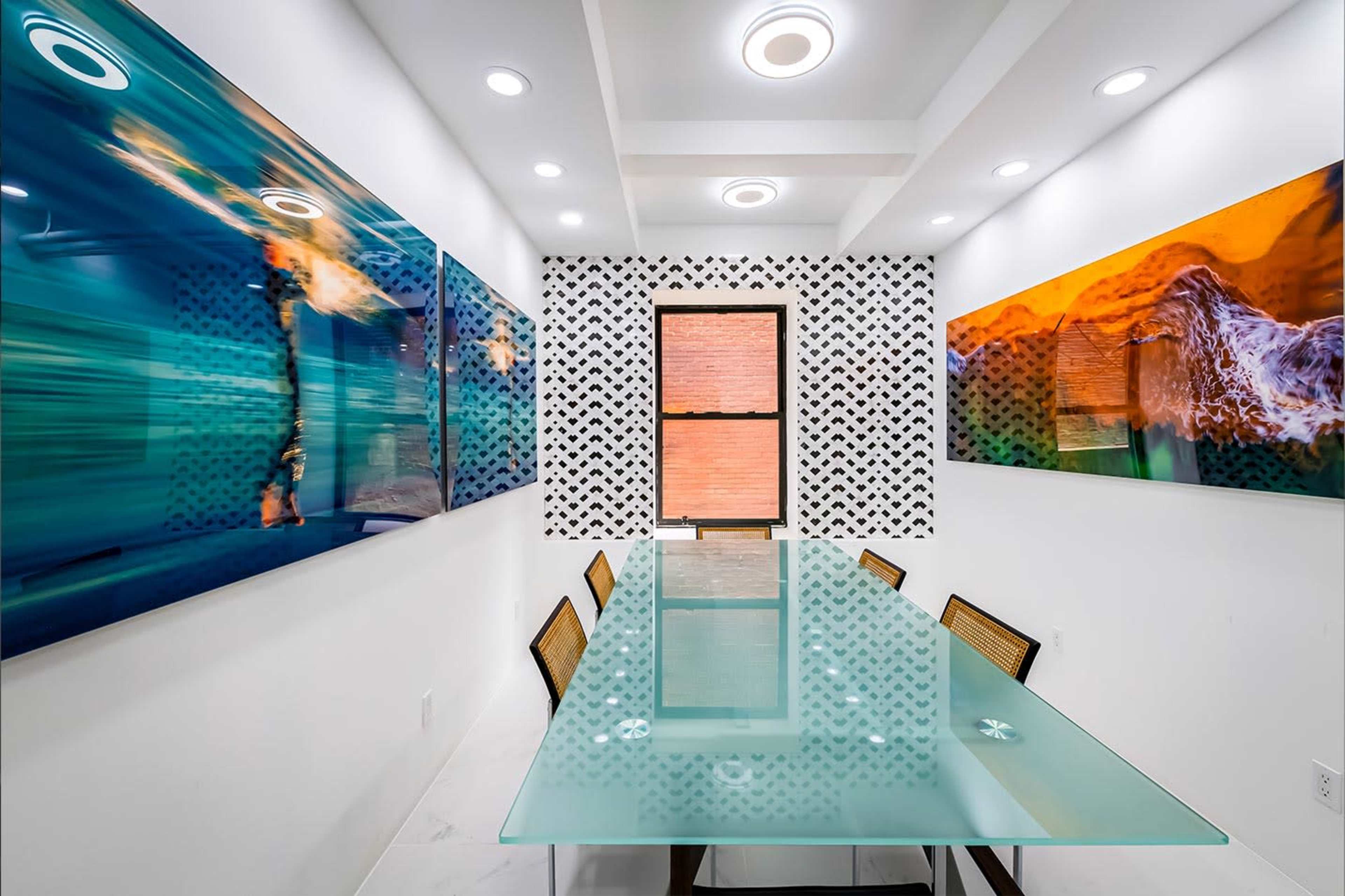 A sleek dining area features a glass table surrounded by rattan chairs, with vibrant abstract artwork displayed on the walls.