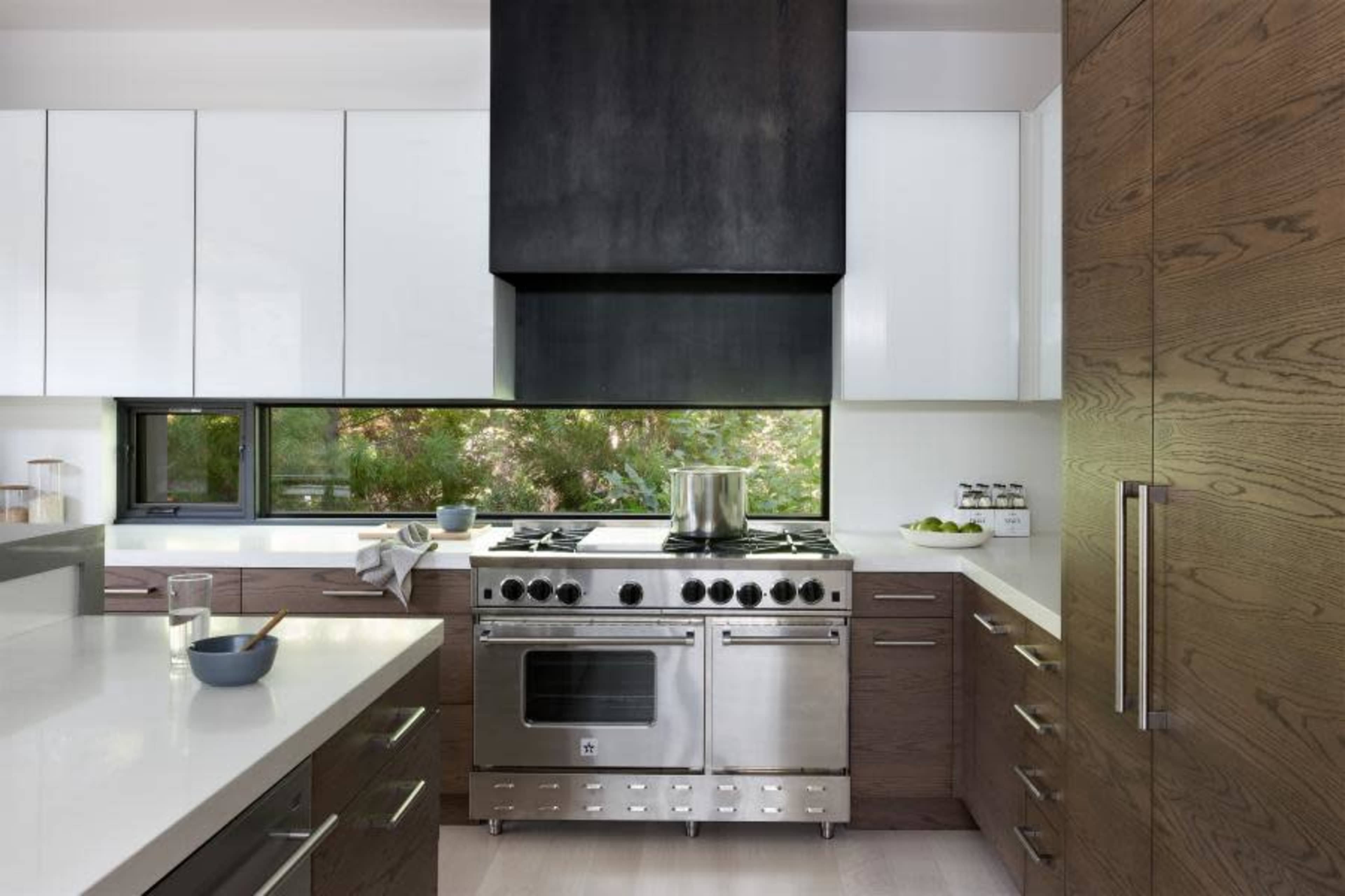 The kitchen features a stainless steel stove under a black hood, with white and dark wood cabinetry and a window providing natural light.