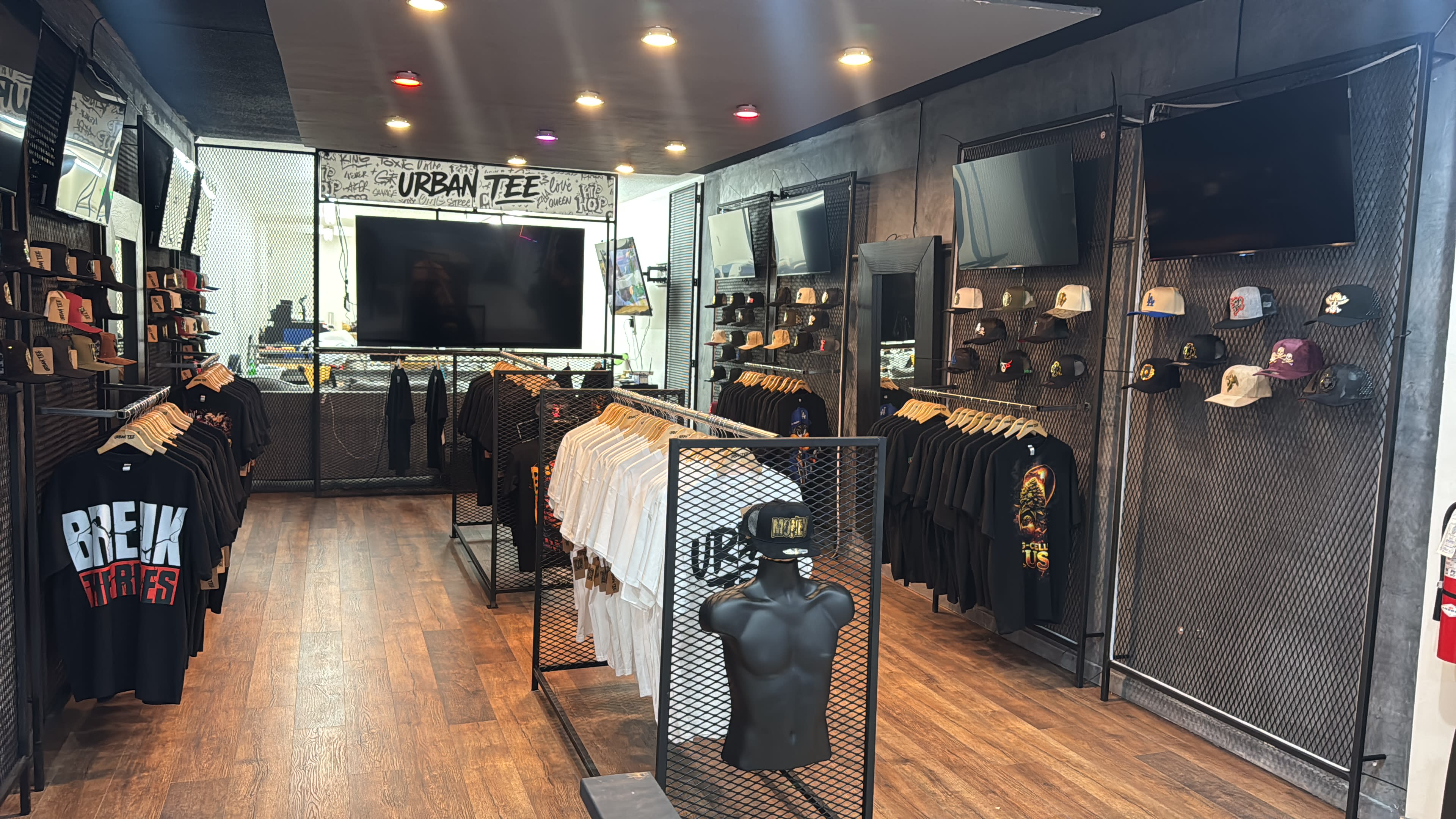 The image shows an urban clothing store with clothing racks displaying graphic t-shirts and hats organized neatly on shelves.