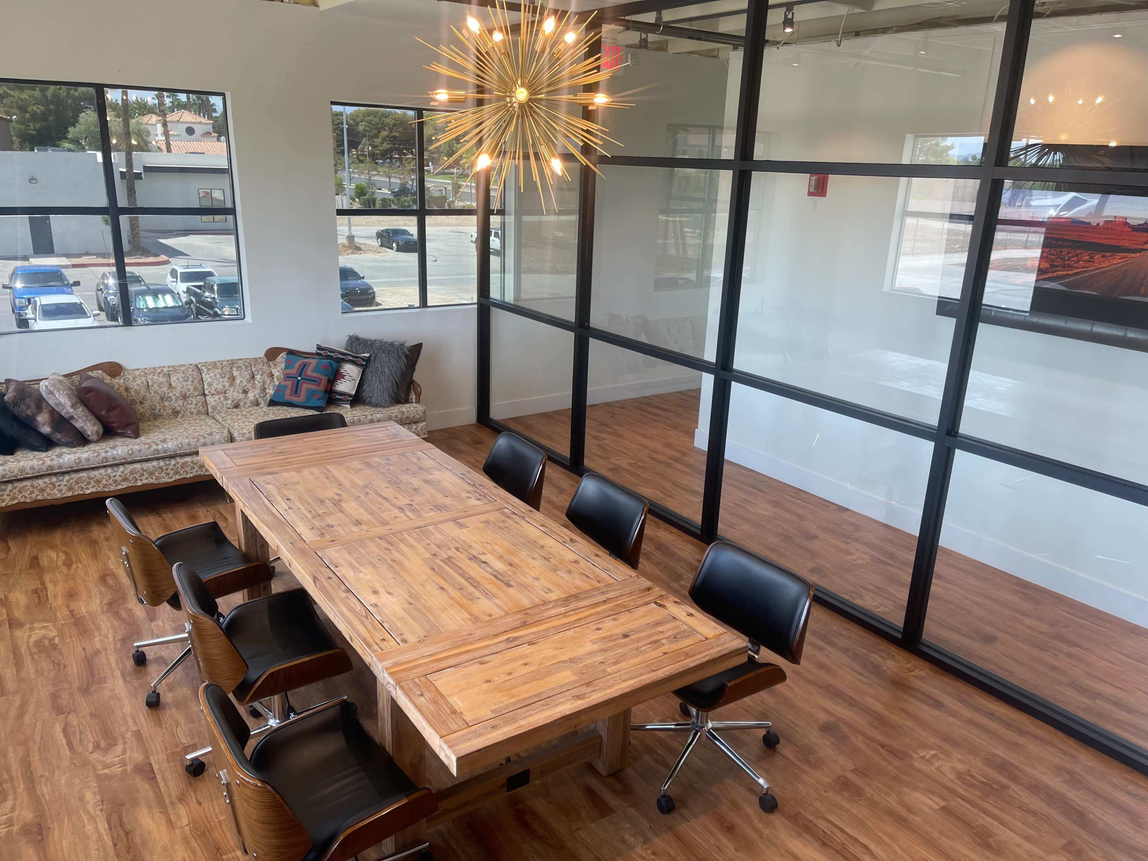 A modern conference room with a large wooden table surrounded by black chairs and a decorative light fixture overhead.