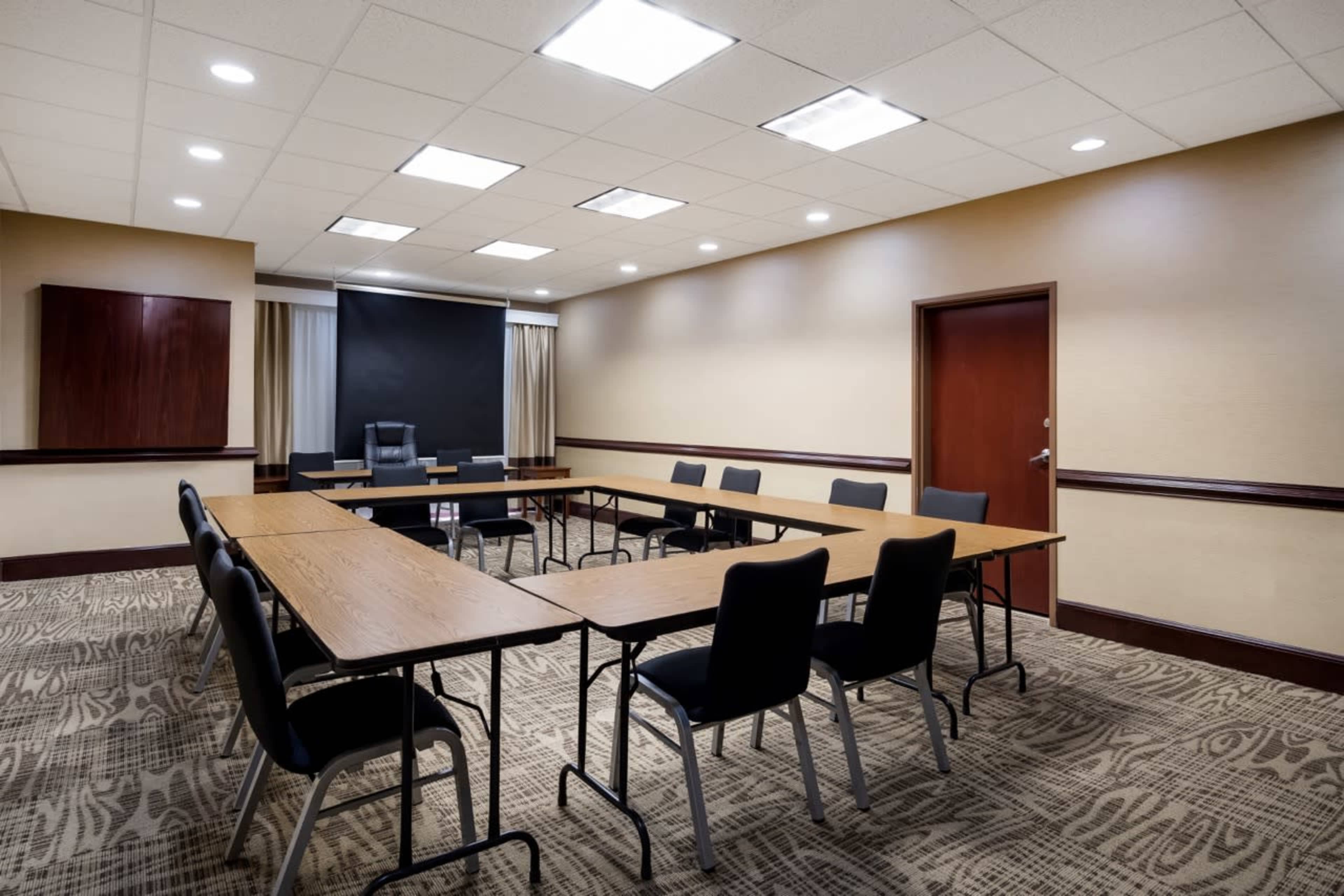 The image shows a conference room with a rectangular table surrounded by chairs and a projector screen at one end.