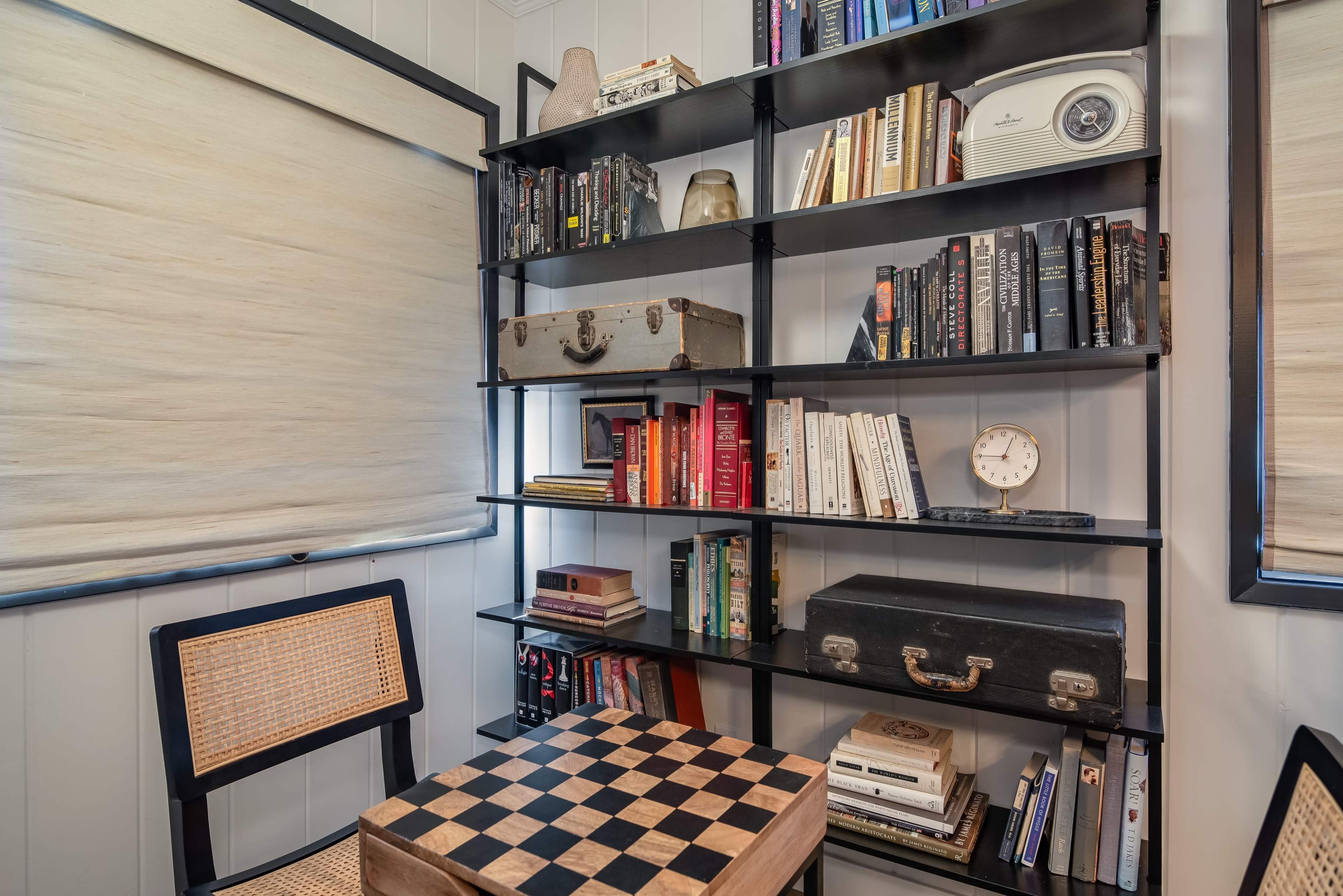 The image shows a small reading nook with a bookshelf filled with various books, a checkered table, and a couple of decorative items on the shelves.