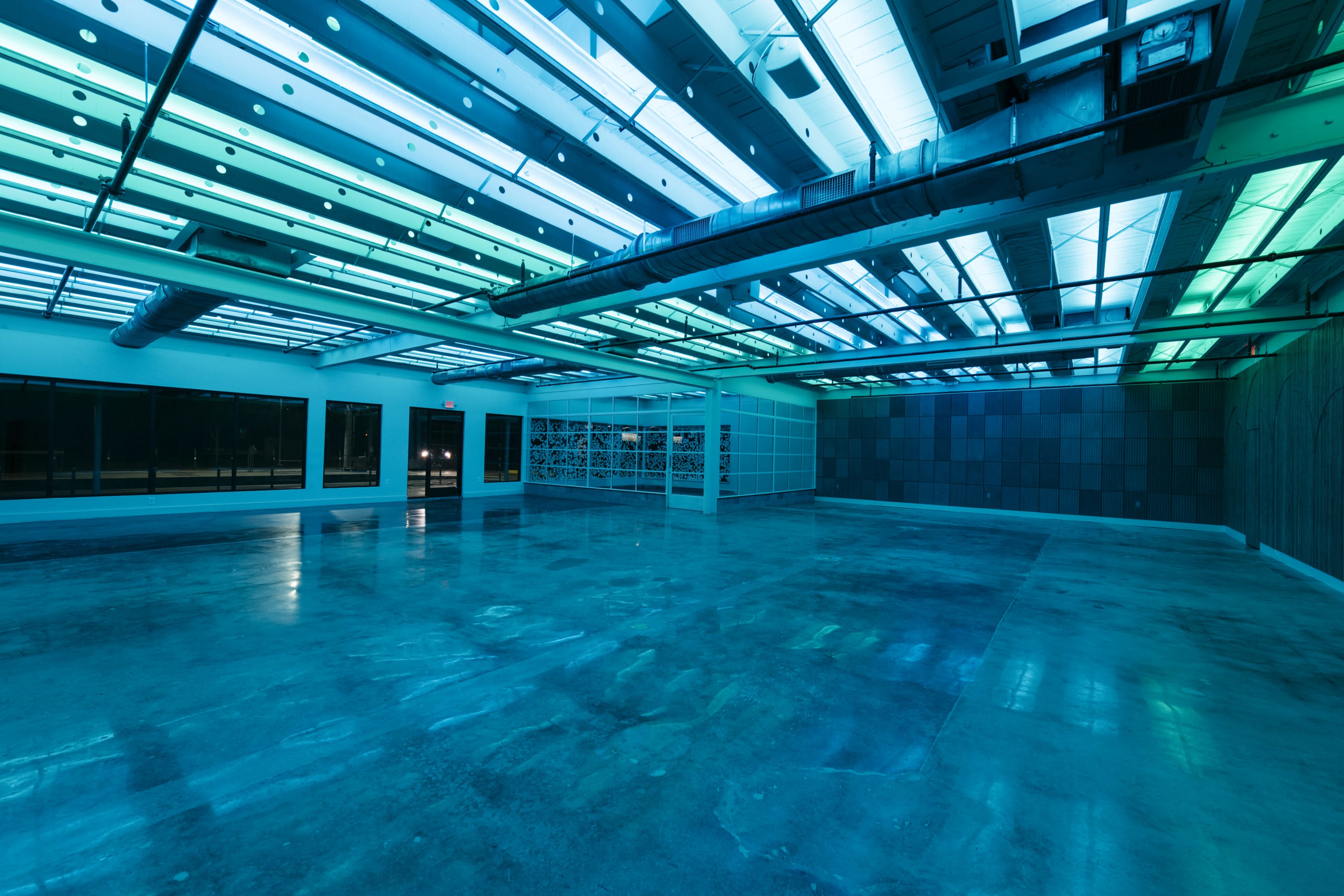 The image shows a large, empty room with polished concrete floors and overhead lights casting a blue-green glow.