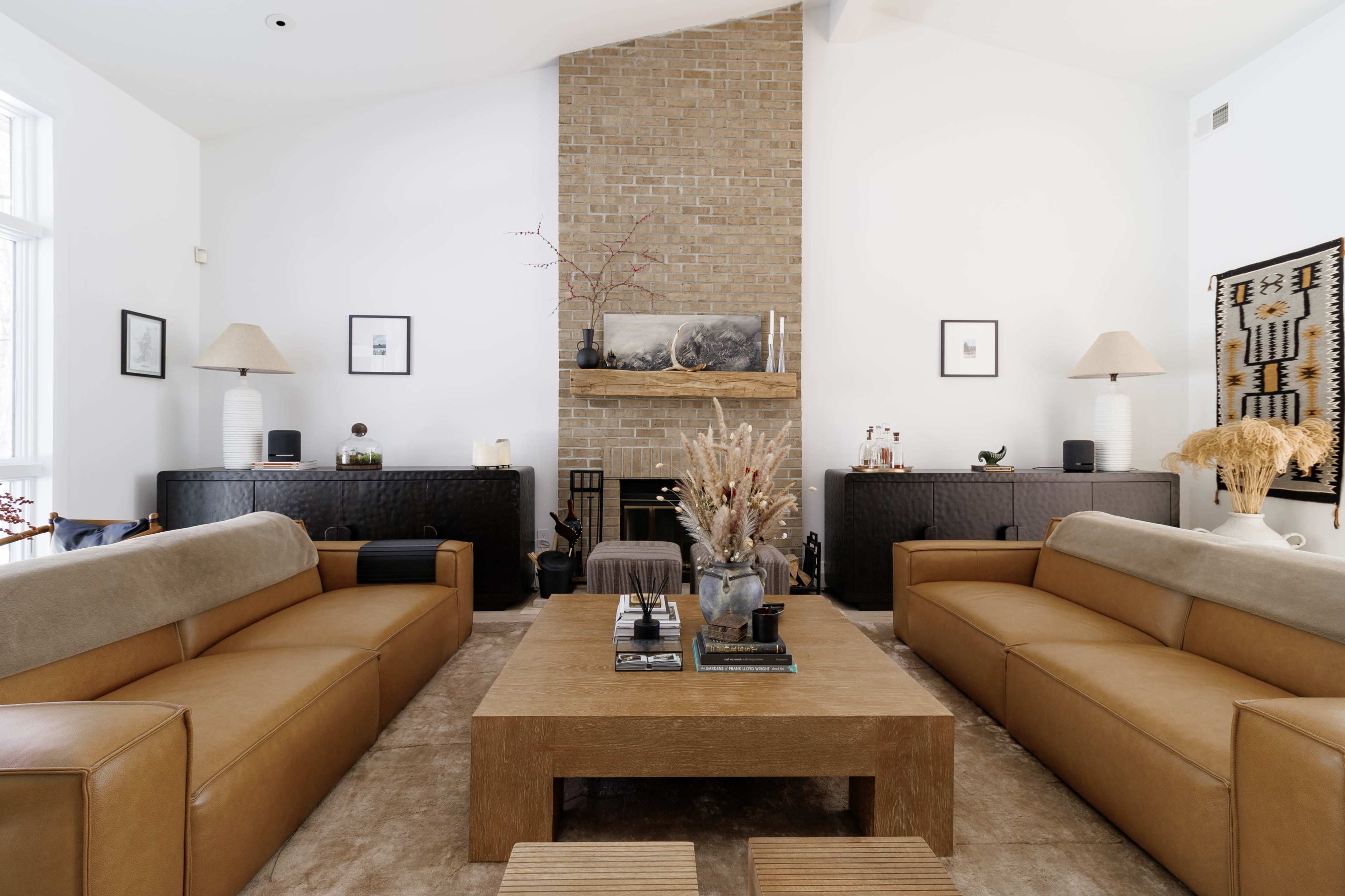 The image shows a modern living room featuring two leather sofas facing a coffee table, with a stone fireplace and decorative elements on the walls and furniture.