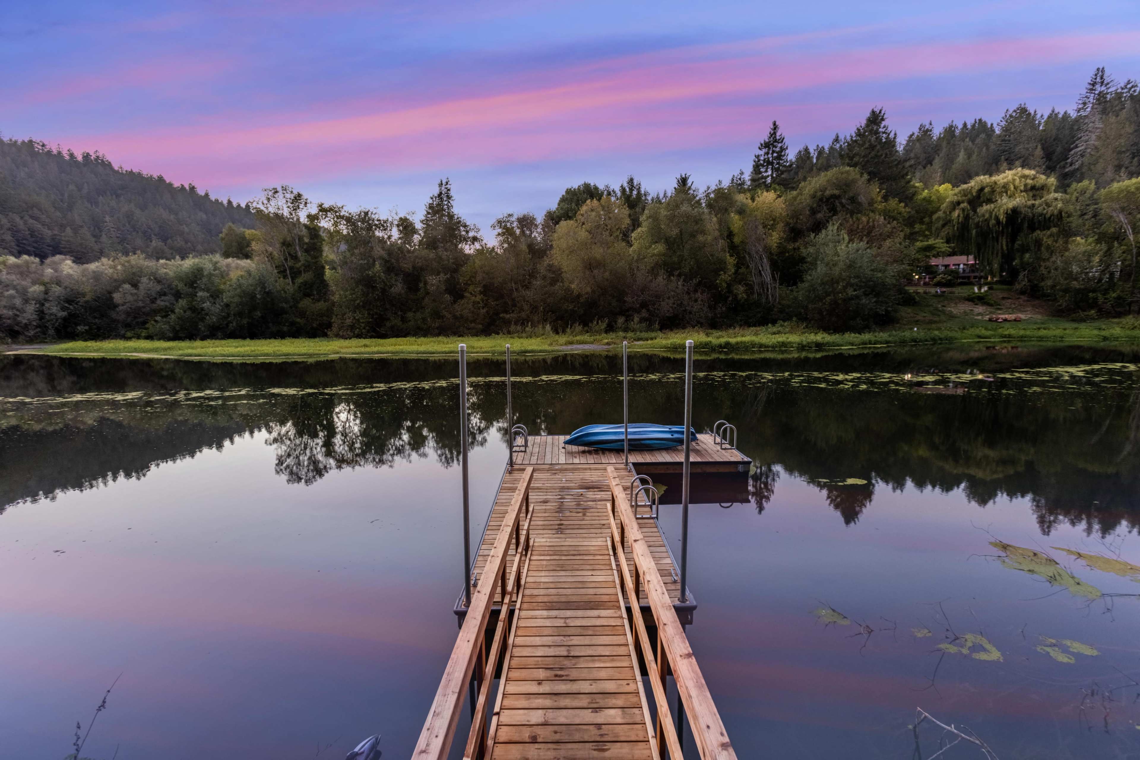 A wooden dock extends into a calm lake surrounded by trees, with a blue kayak resting nearby.