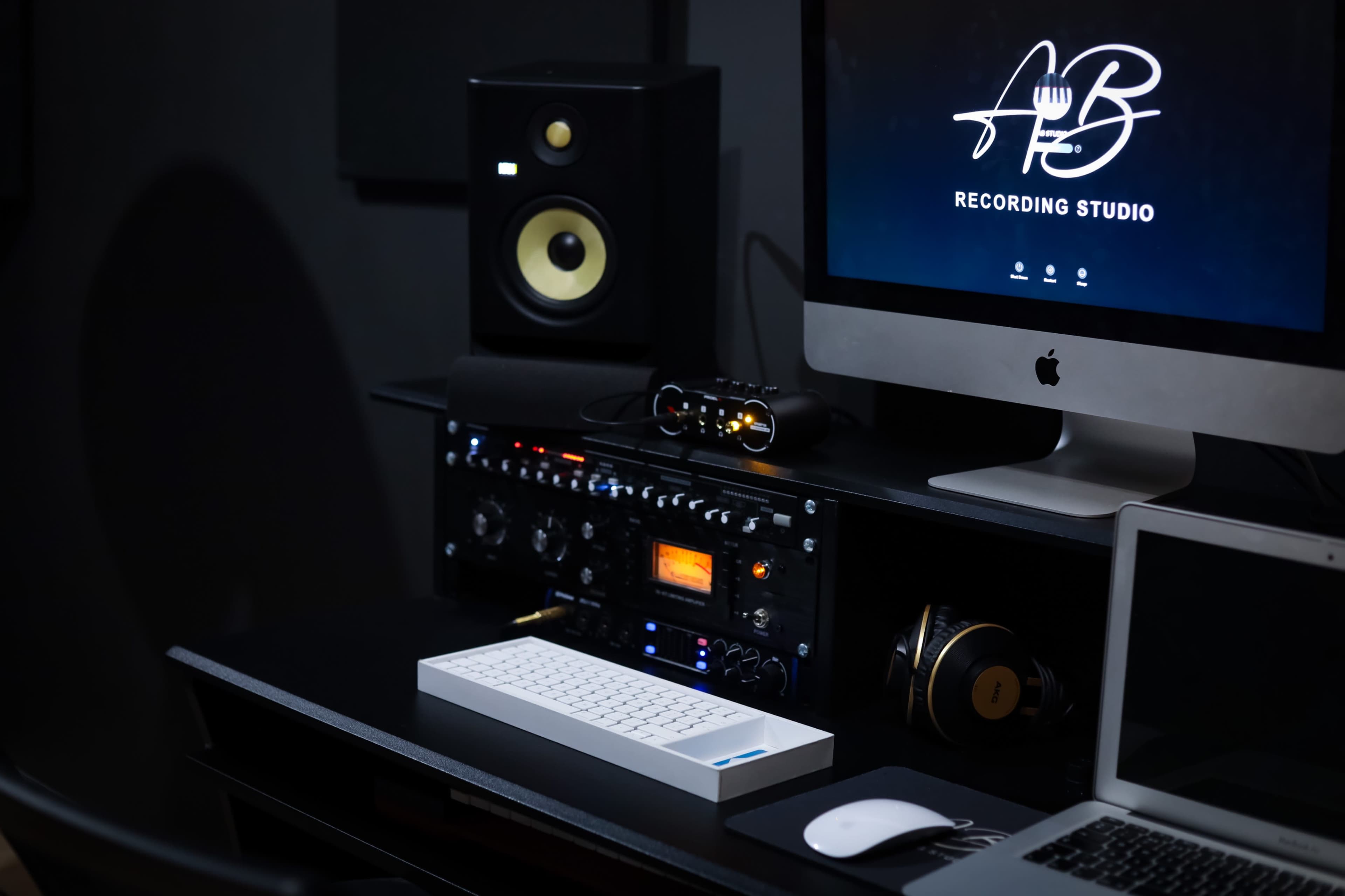 The image shows a recording studio setup featuring a computer monitor, audio equipment, and a keyboard on a desk.