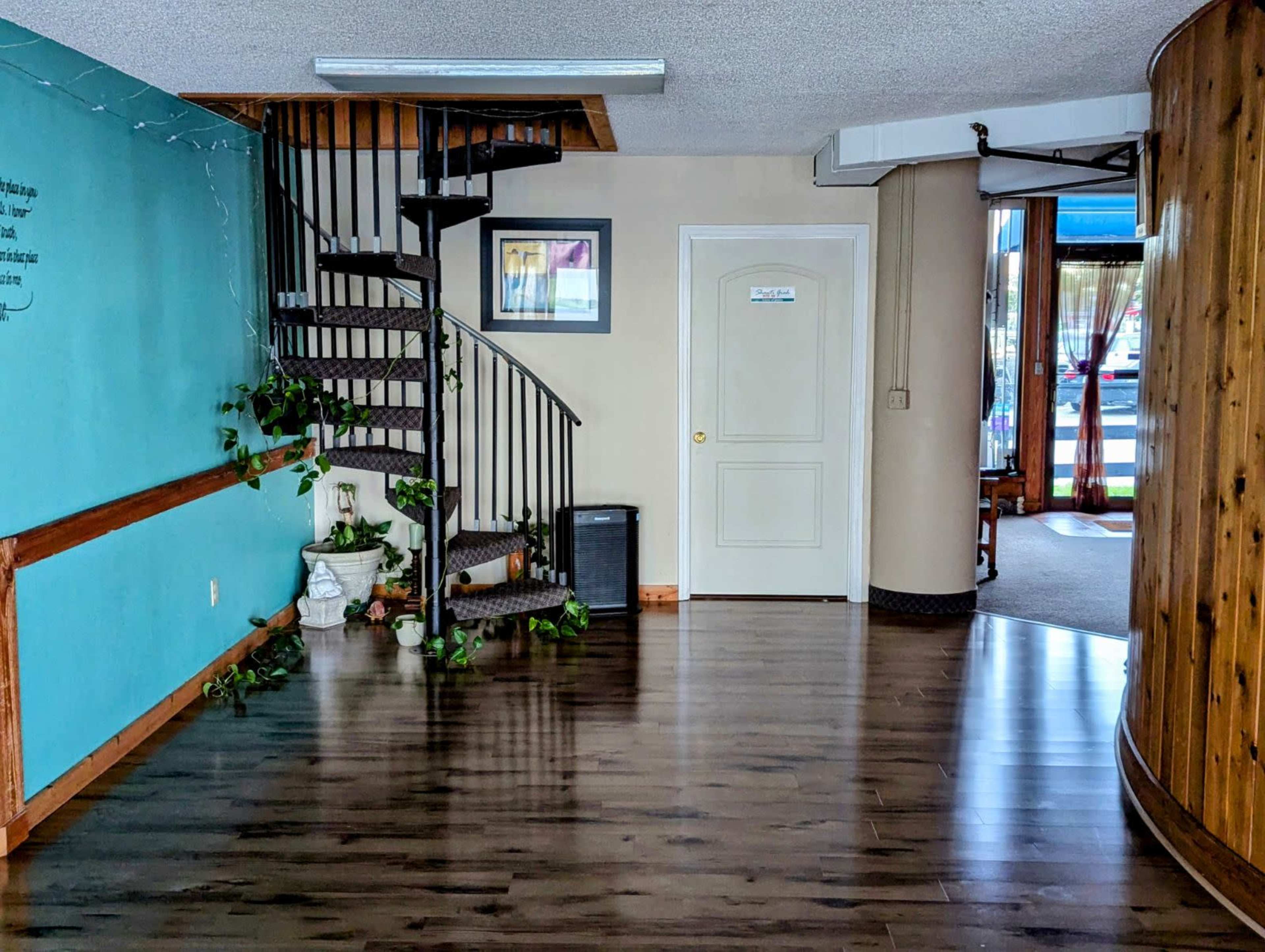 The image shows a spacious entryway with a spiral staircase on the left, a blue accent wall adorned with green plants, and a door on the right leading to another room.