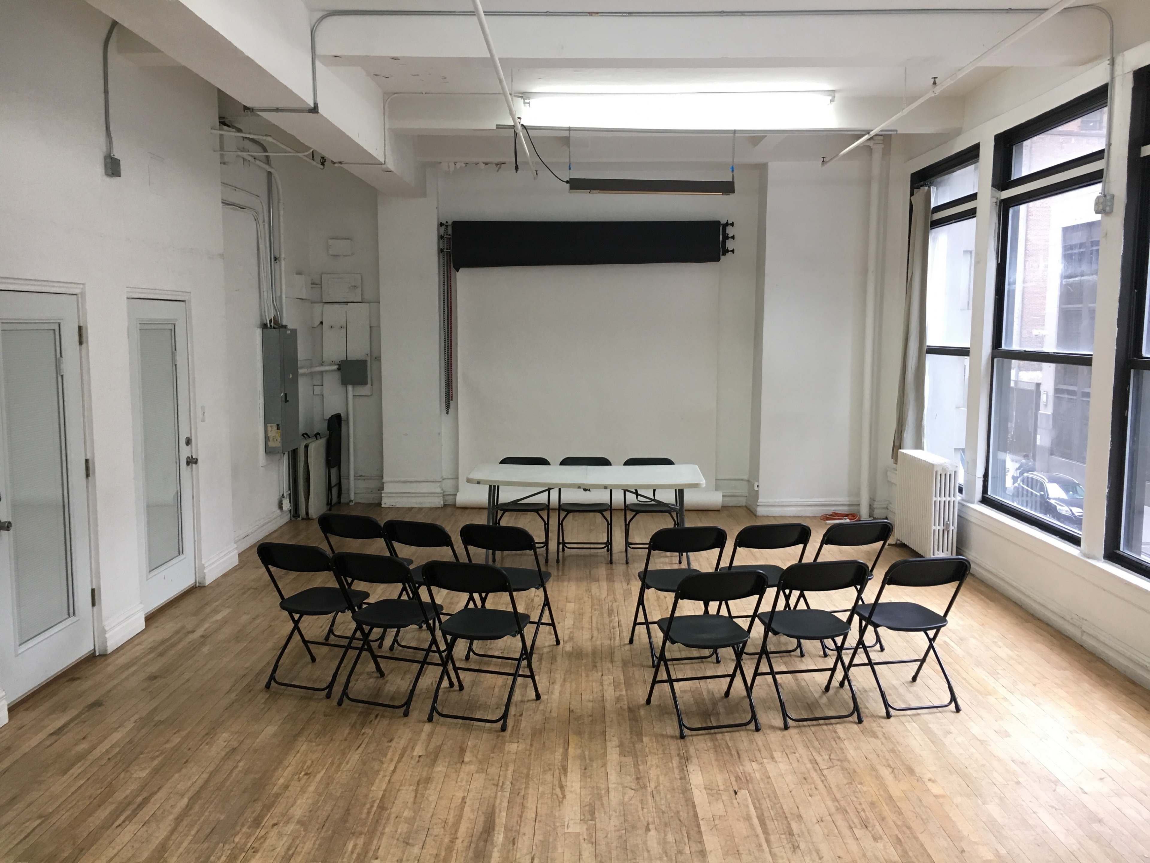 A simple room with a white backdrop and a long table surrounded by folding chairs arranged in a semicircle.