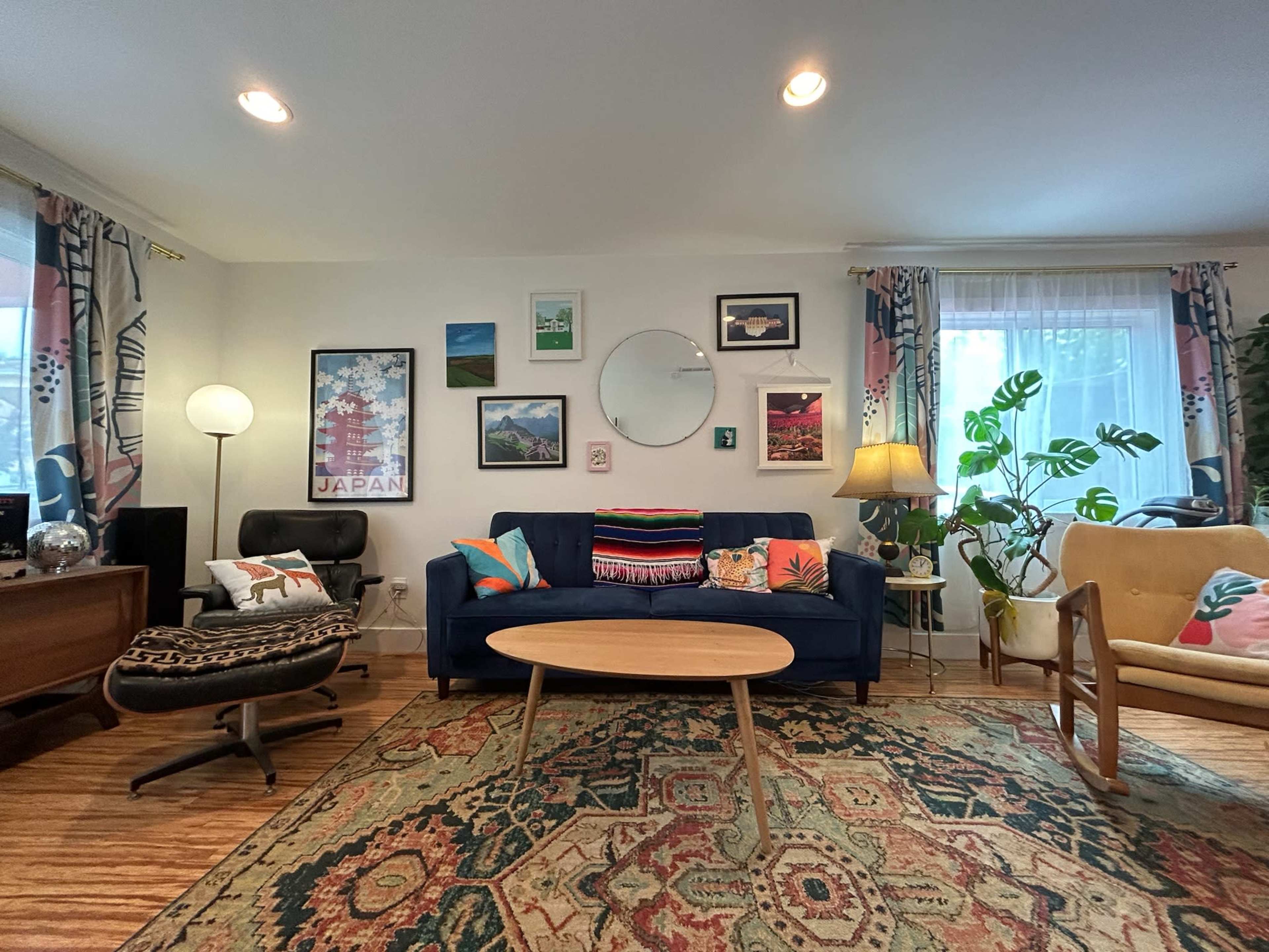 The living room features a blue couch with assorted cushions, a round coffee table, and various framed artworks on the walls, complemented by plants and additional seating.