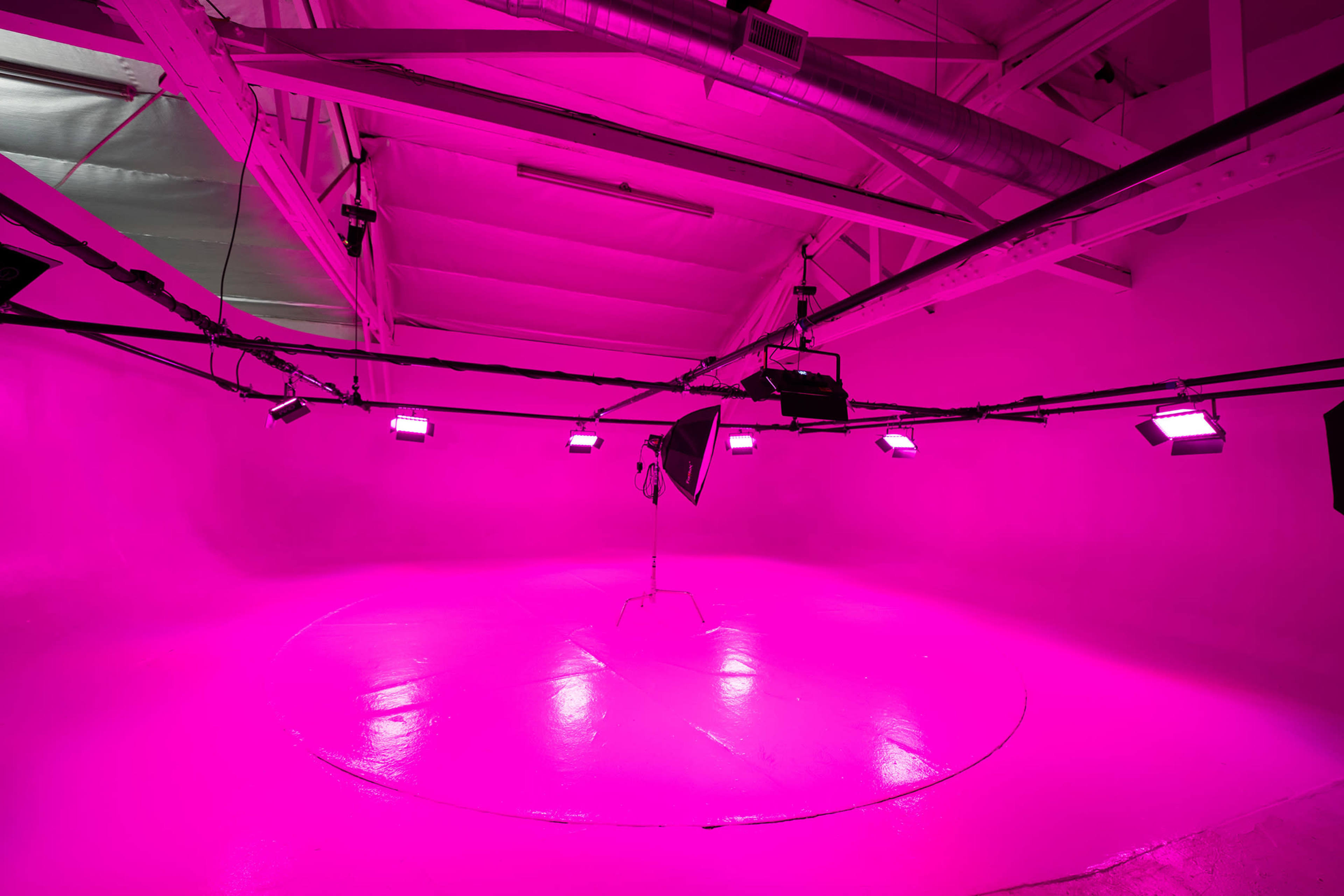 A studio space with bright pink walls and lighting, featuring a central platform and a single light stand.