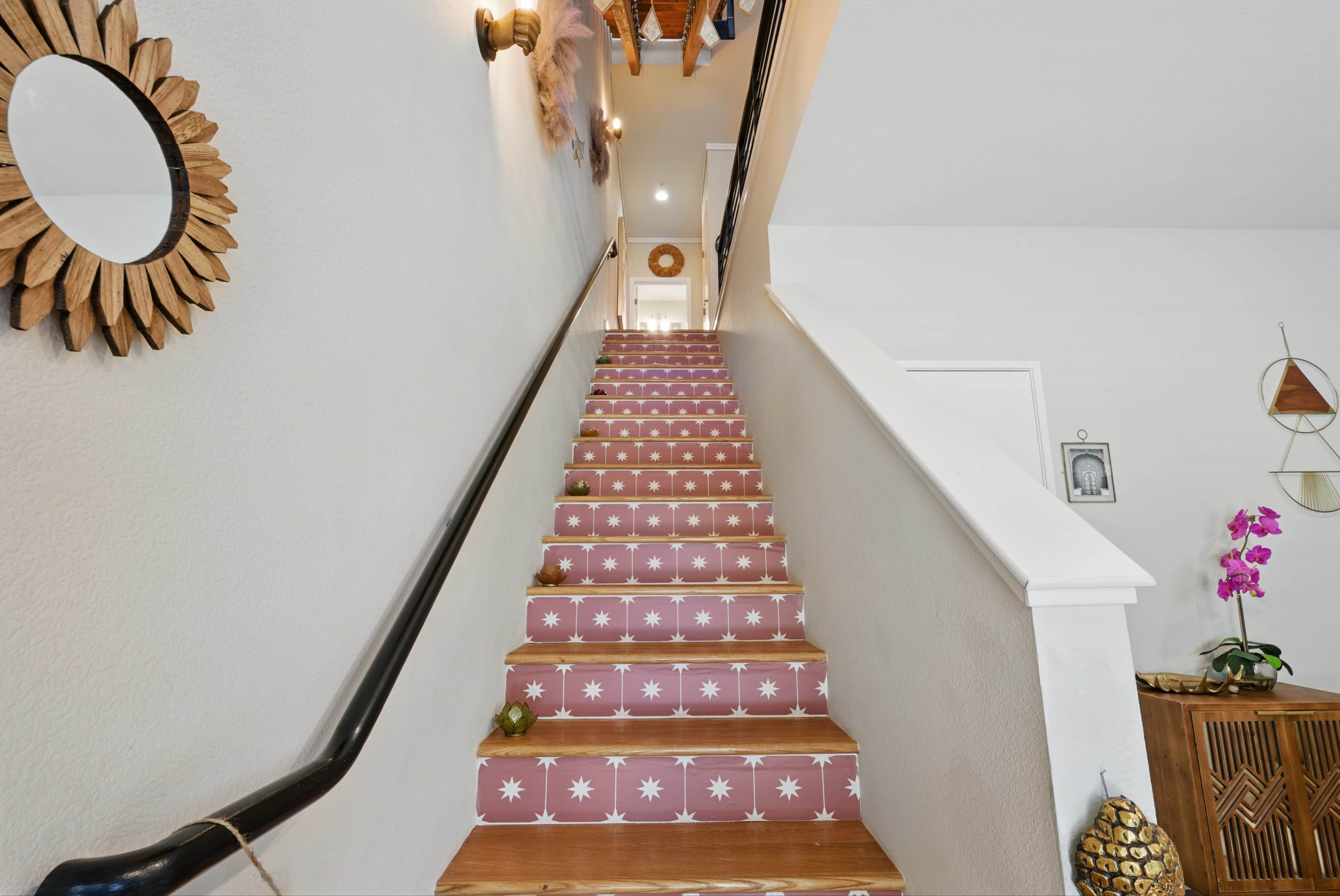 A staircase with decorated risers featuring a pink and white star pattern leads upward, flanked by a wall mirror and decorative elements.