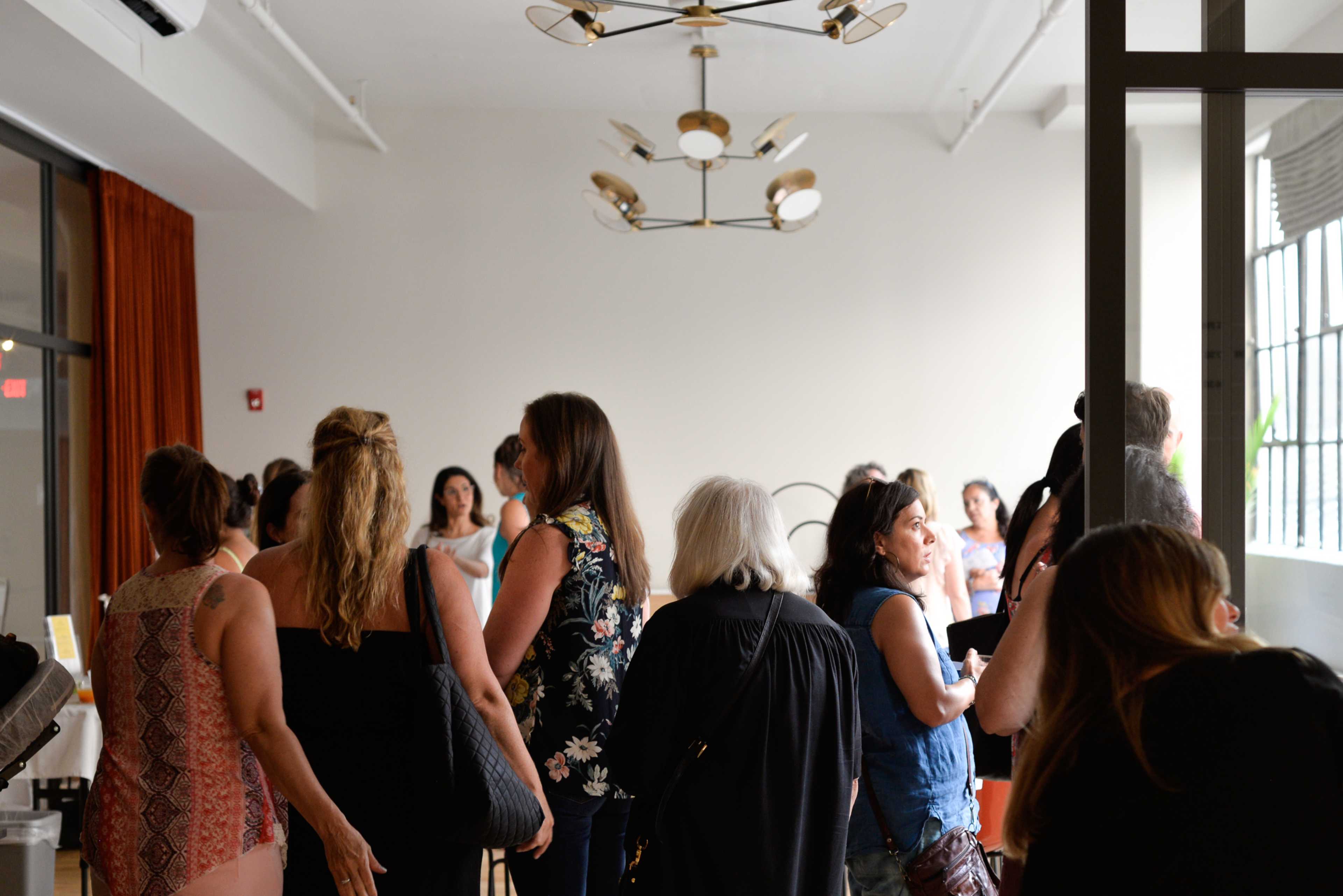 A group of people is gathered in a spacious indoor area with large windows and modern lighting fixtures.