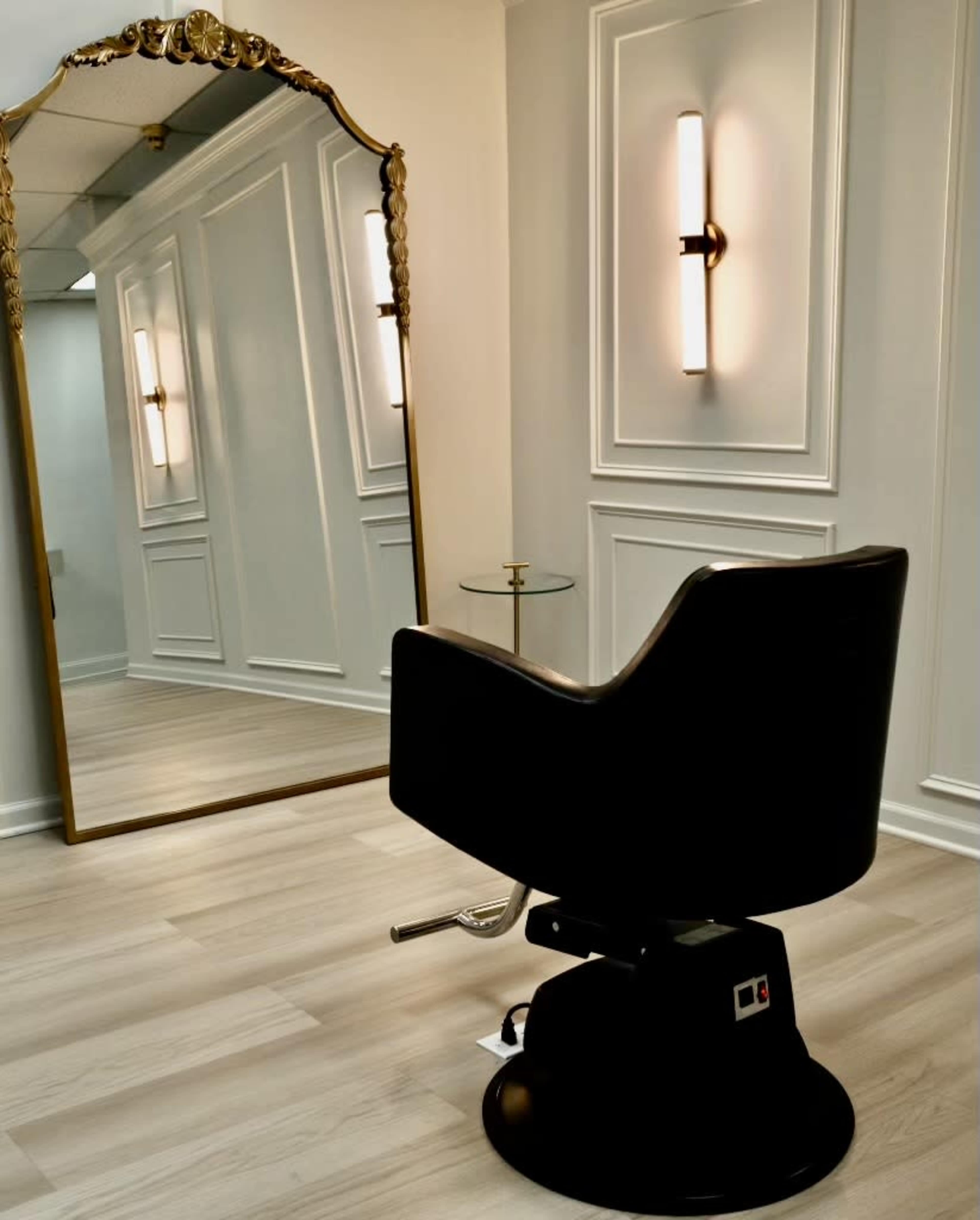 The image shows a modern hair salon interior with a stylist's chair positioned in front of a large decorative mirror and wall sconces.