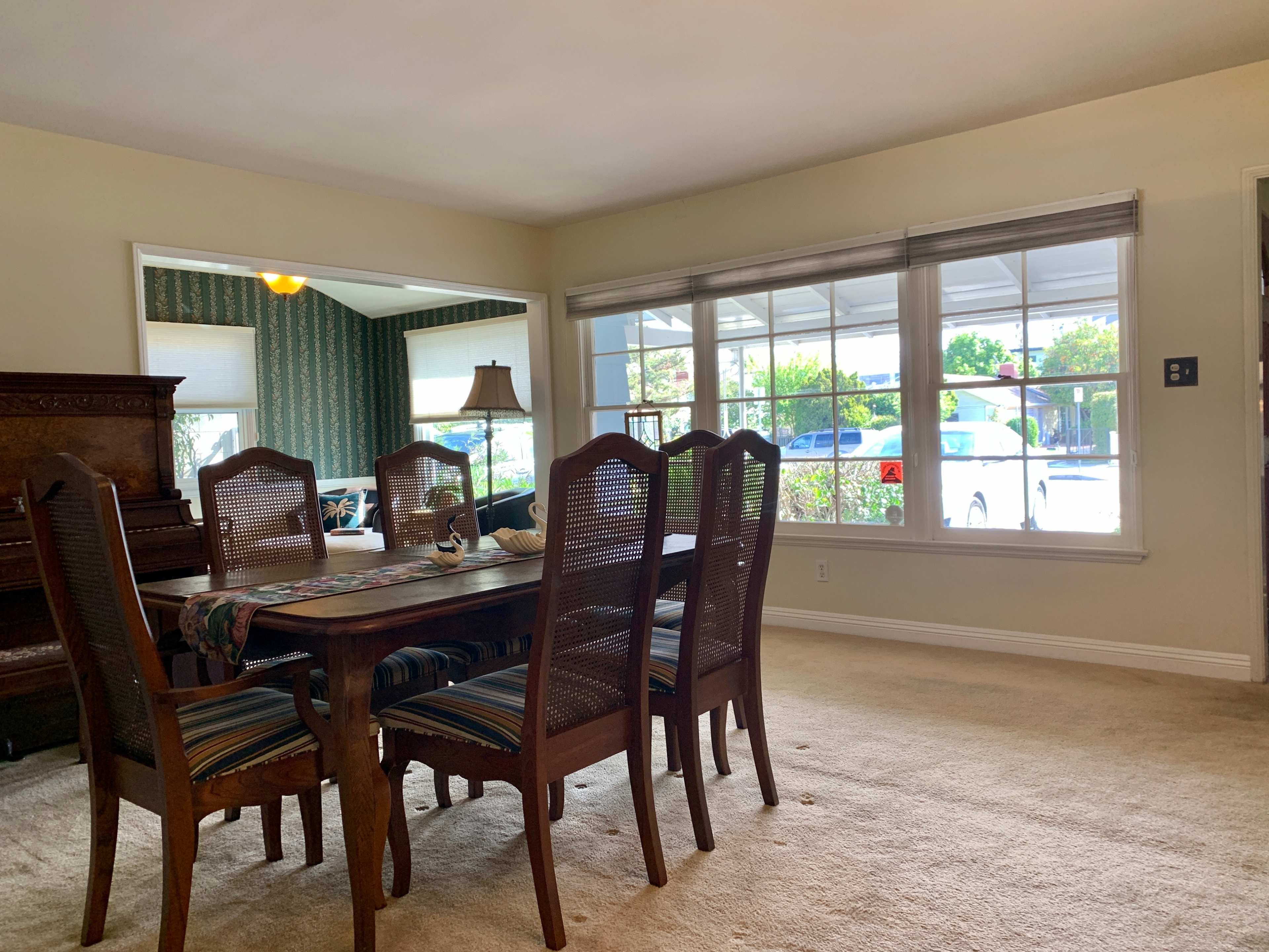 A dining room with a wooden table surrounded by chairs and large windows letting in natural light.
