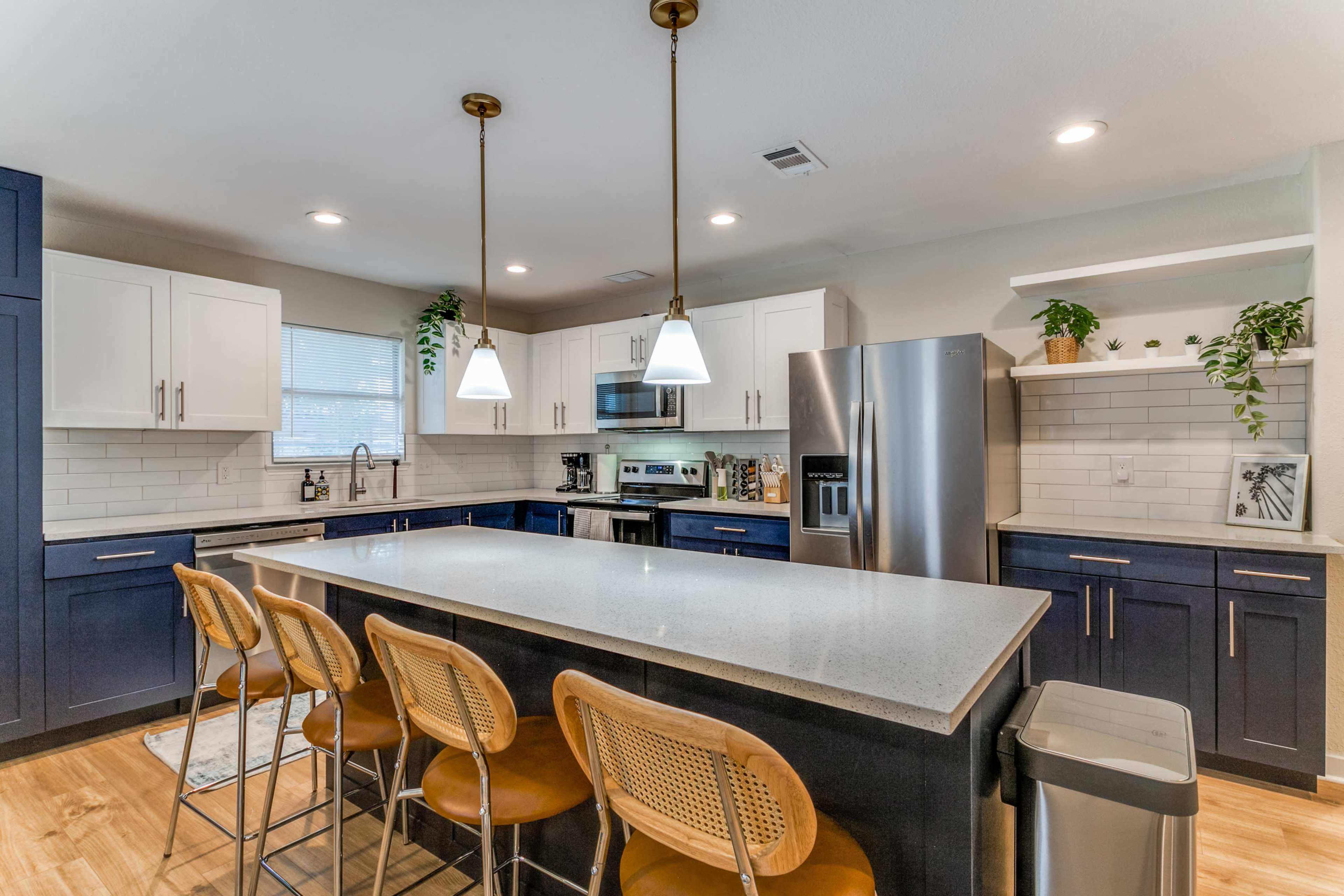 A modern kitchen featuring a central island with four wicker barstools, stainless steel appliances, and white and navy cabinetry.