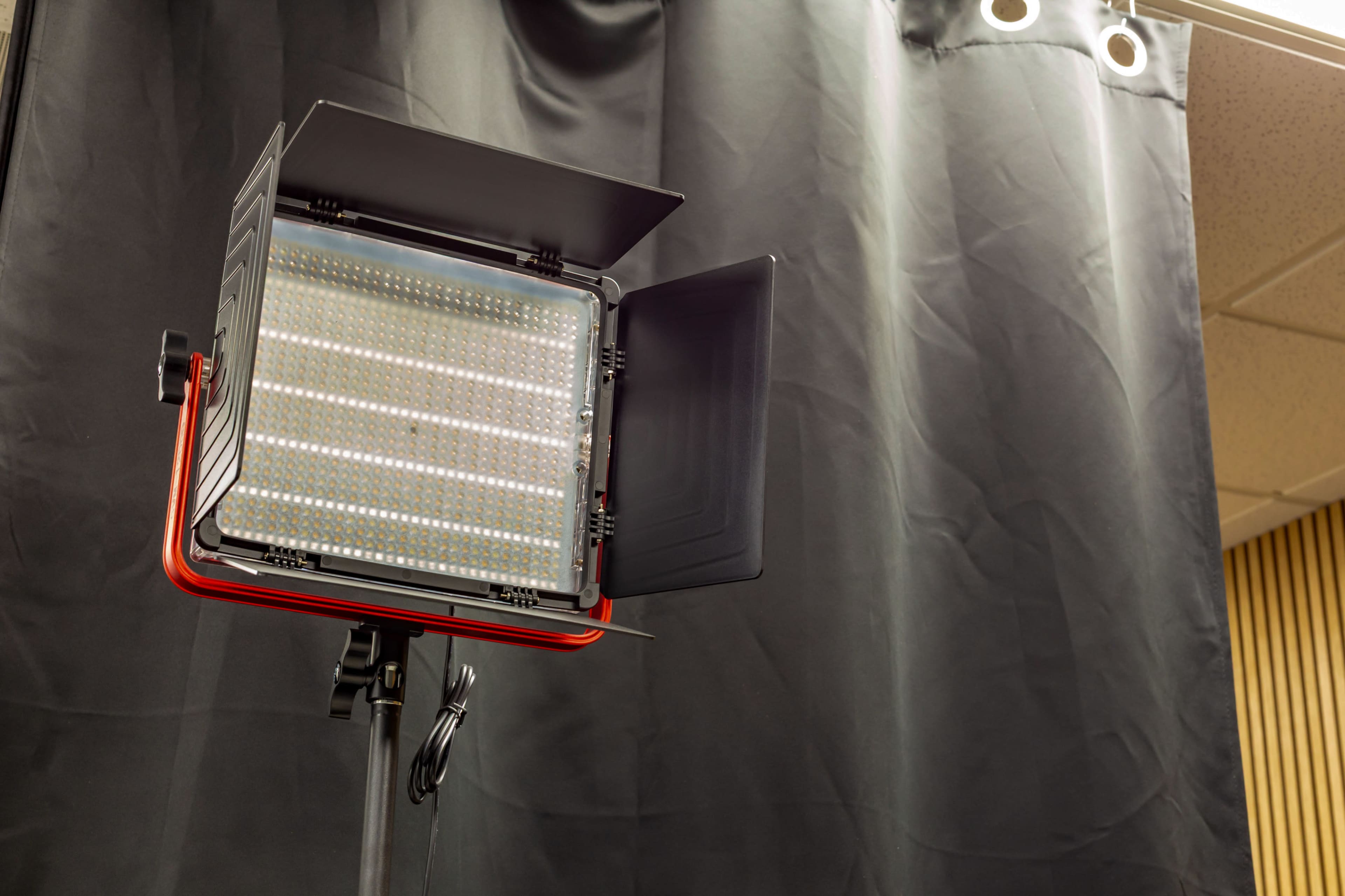 A professional LED studio light is positioned against a black backdrop with curtains.