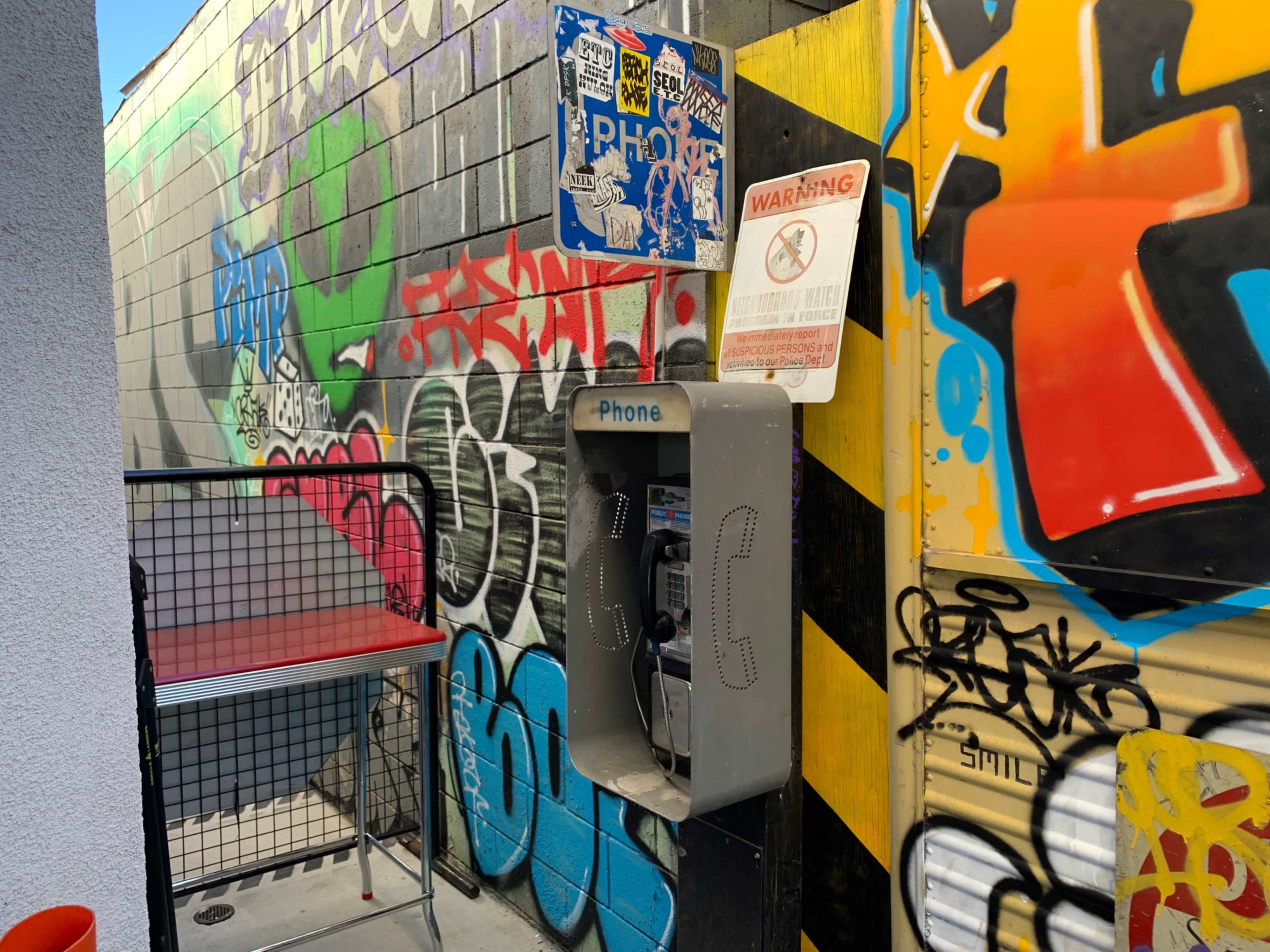 A payphone mounted on a colorful, graffiti-covered wall in a narrow alley.