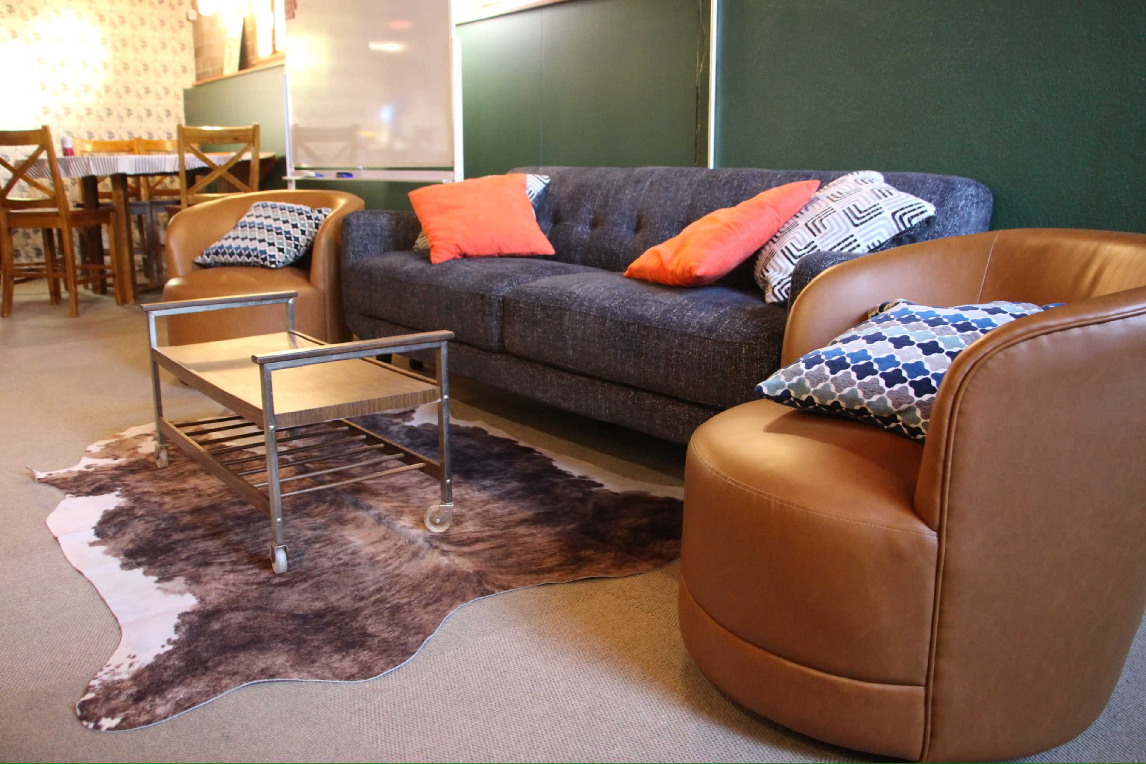 The image shows a stylish seating area featuring a gray upholstered sofa, two curved brown chairs, and a metal coffee table on a cowhide rug.