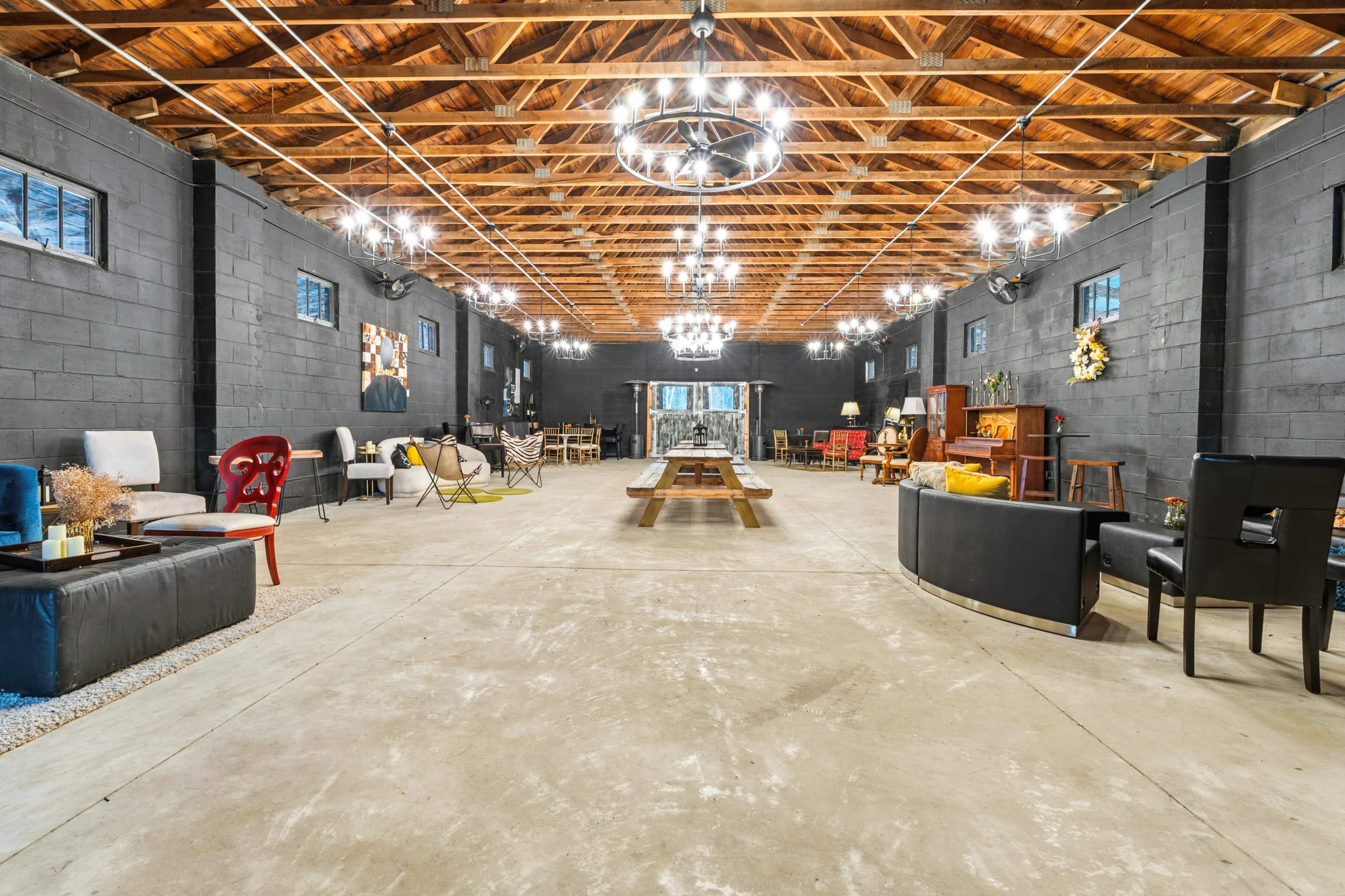 The image shows a spacious industrial-style interior with high wooden ceilings, exposed beams, and various seating arrangements scattered throughout the room.